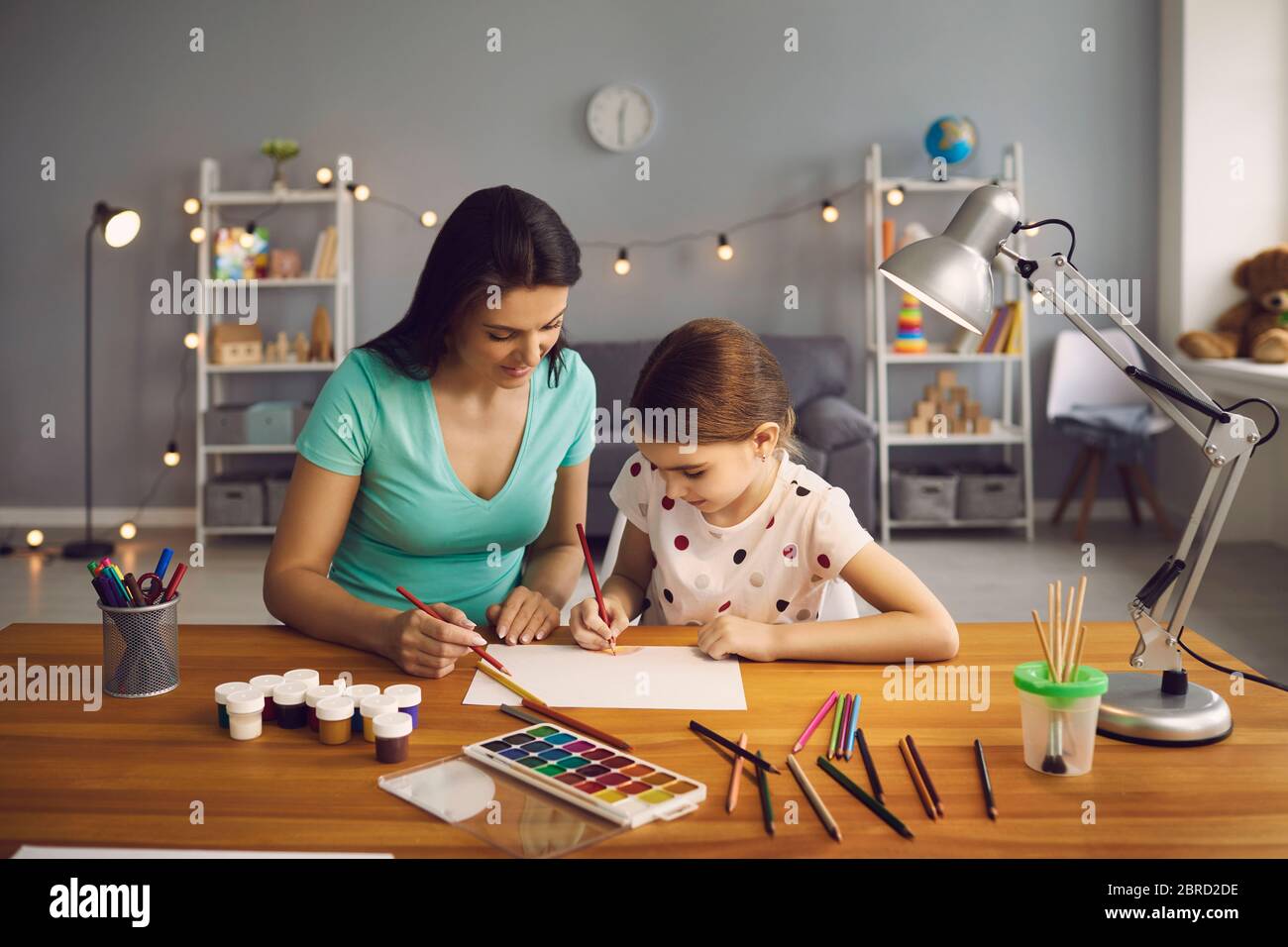 Frohe Familie. Das Kind zieht. Kleines Mädchen und Mutter zeichnen auf dem Tisch im Zimmer. Mutter lehrt Tochter zu zeichnen, während sitzen am Tisch zu Hause. Stockfoto