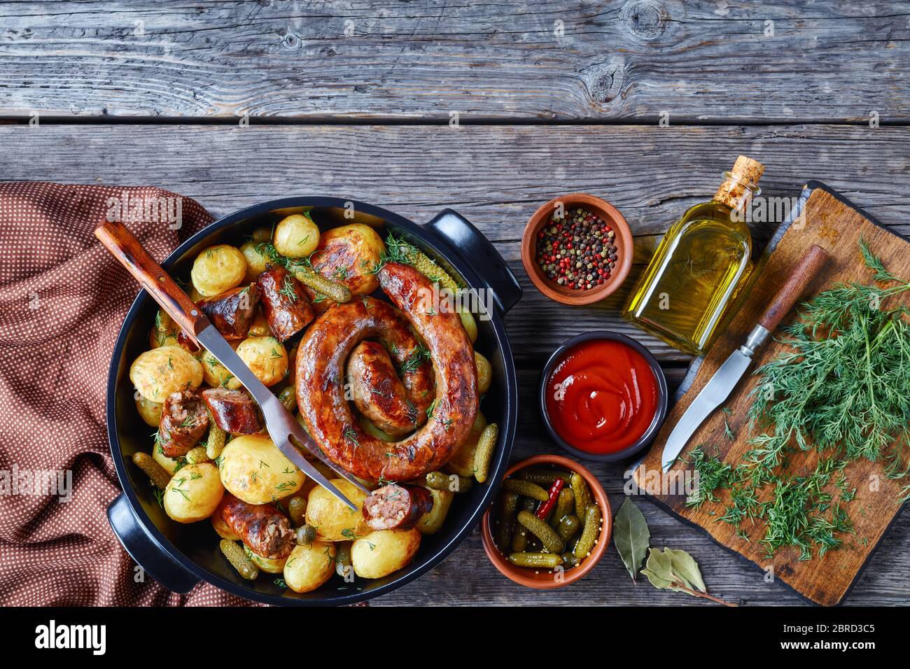 Hausgemachte britische Mahlzeit: Gebratene Schweinewurst und junge Kartoffel mit Gurken, bestreut mit frischem Dill auf einem schwarzen Gericht auf einem hölzernen Hintergrund mit Ketc Stockfoto