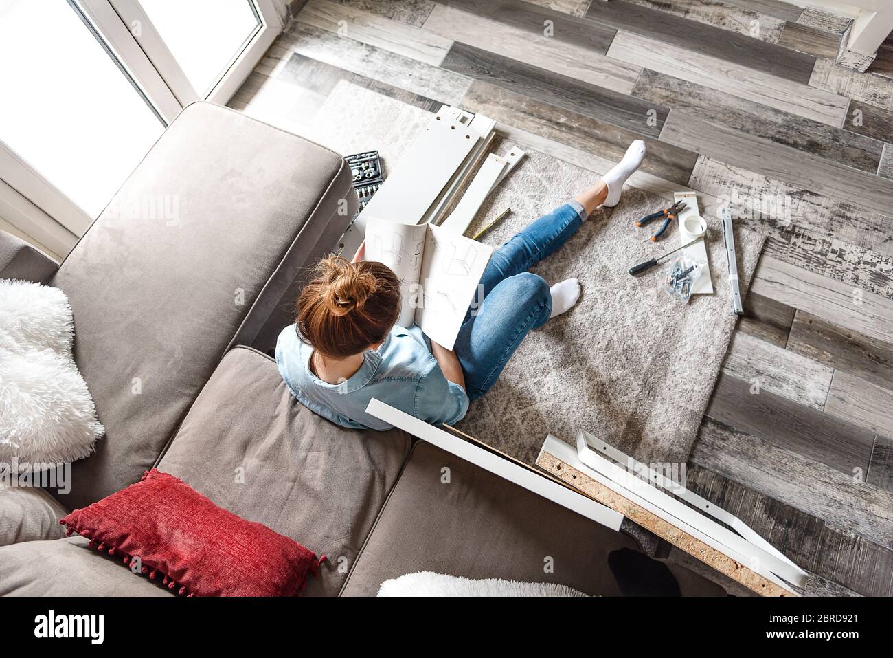 Konzentrierte junge Frau liest die Anweisungen, Möbel zu Hause im Wohnzimmer zu montieren Stockfoto
