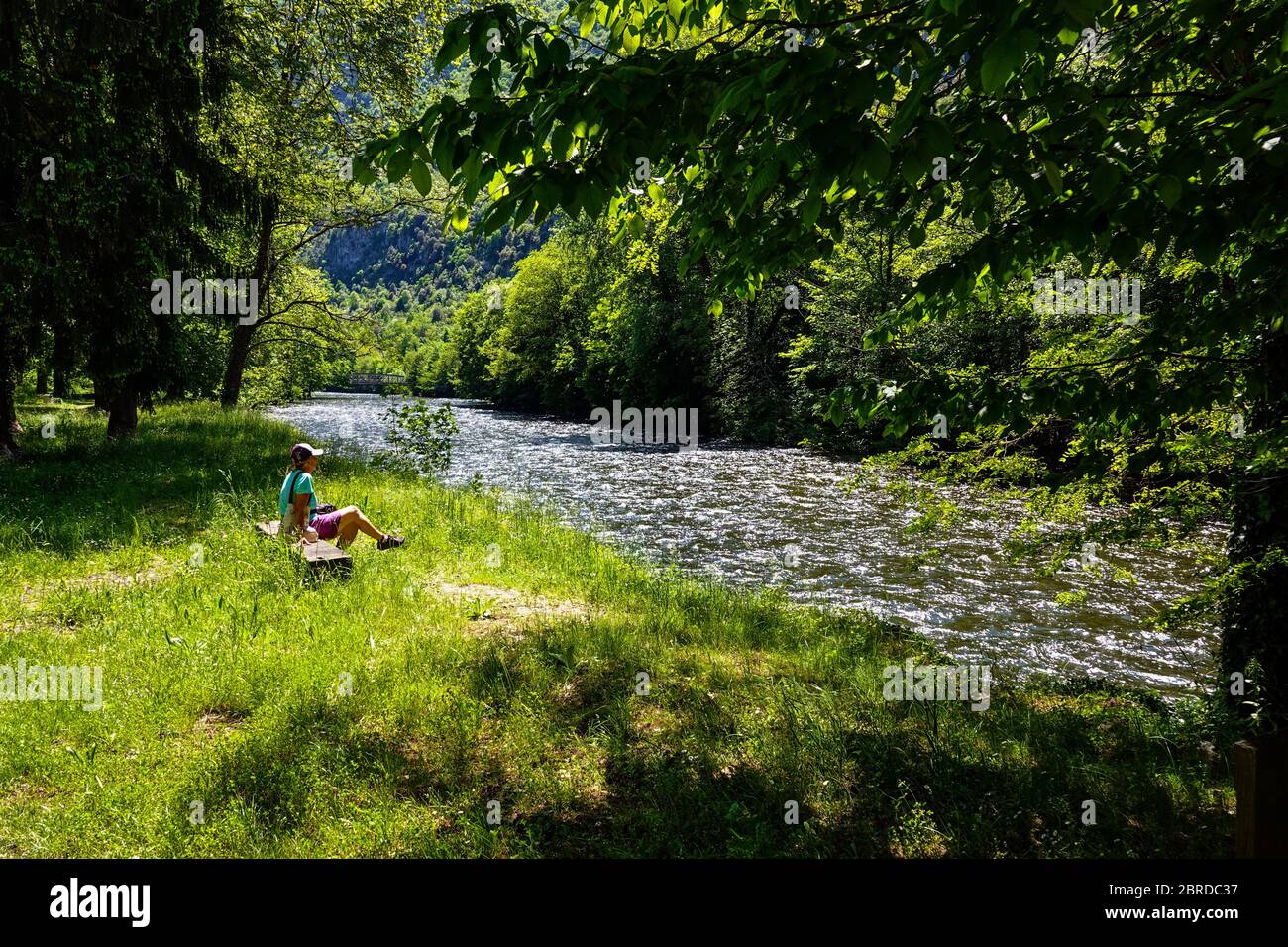 Einsame Frau sitzt am Fluss, mit Frühlingsgrün und der Ariege Fluss fließt durch die Pyrenäen, Ariege, Französisch Pyrenäen, Frankreich Stockfoto