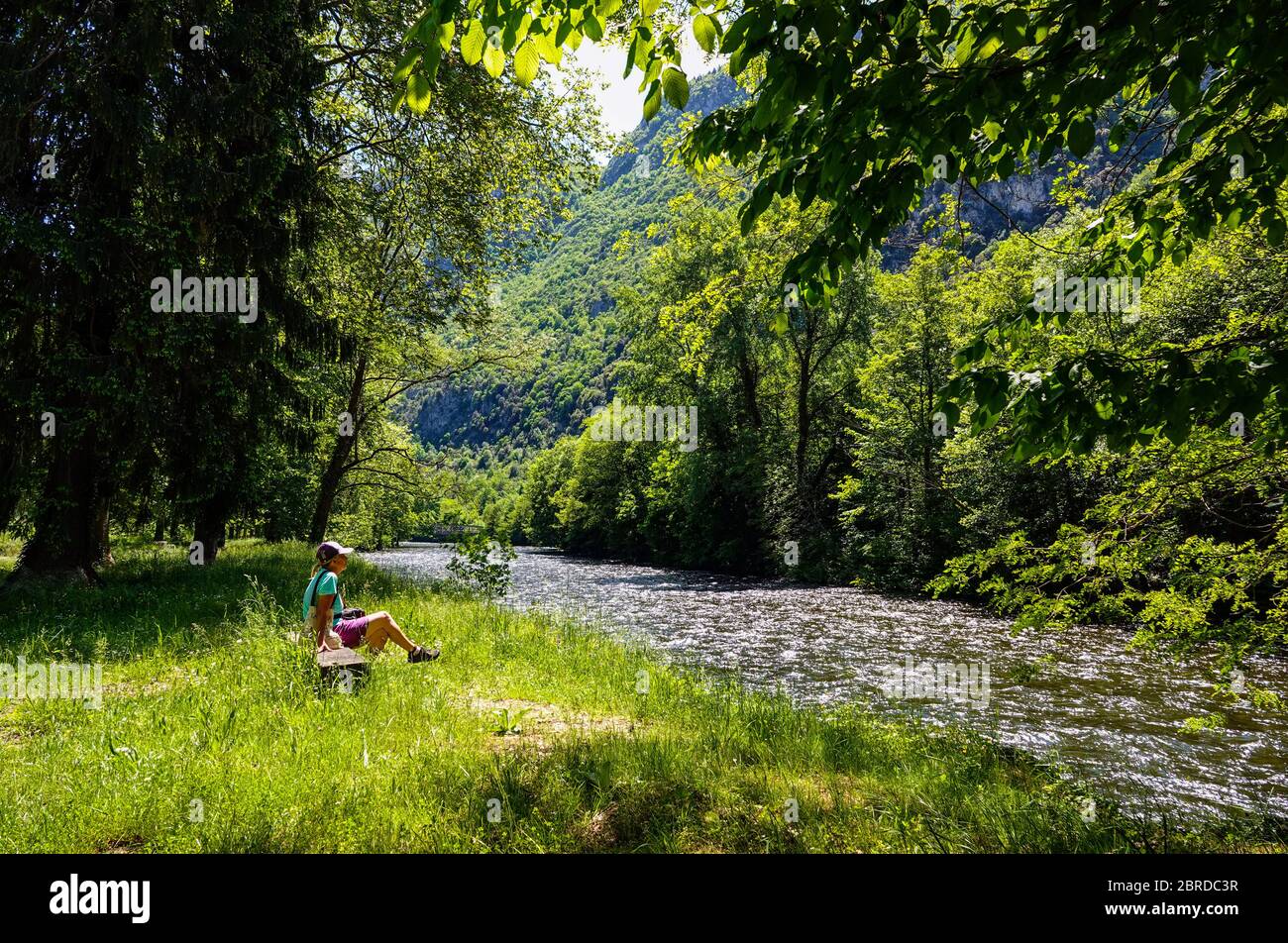 Einsame Frau sitzt am Fluss, mit Frühlingsgrün und der Ariege Fluss fließt durch die Pyrenäen, Ariege, Französisch Pyrenäen, Frankreich Stockfoto
