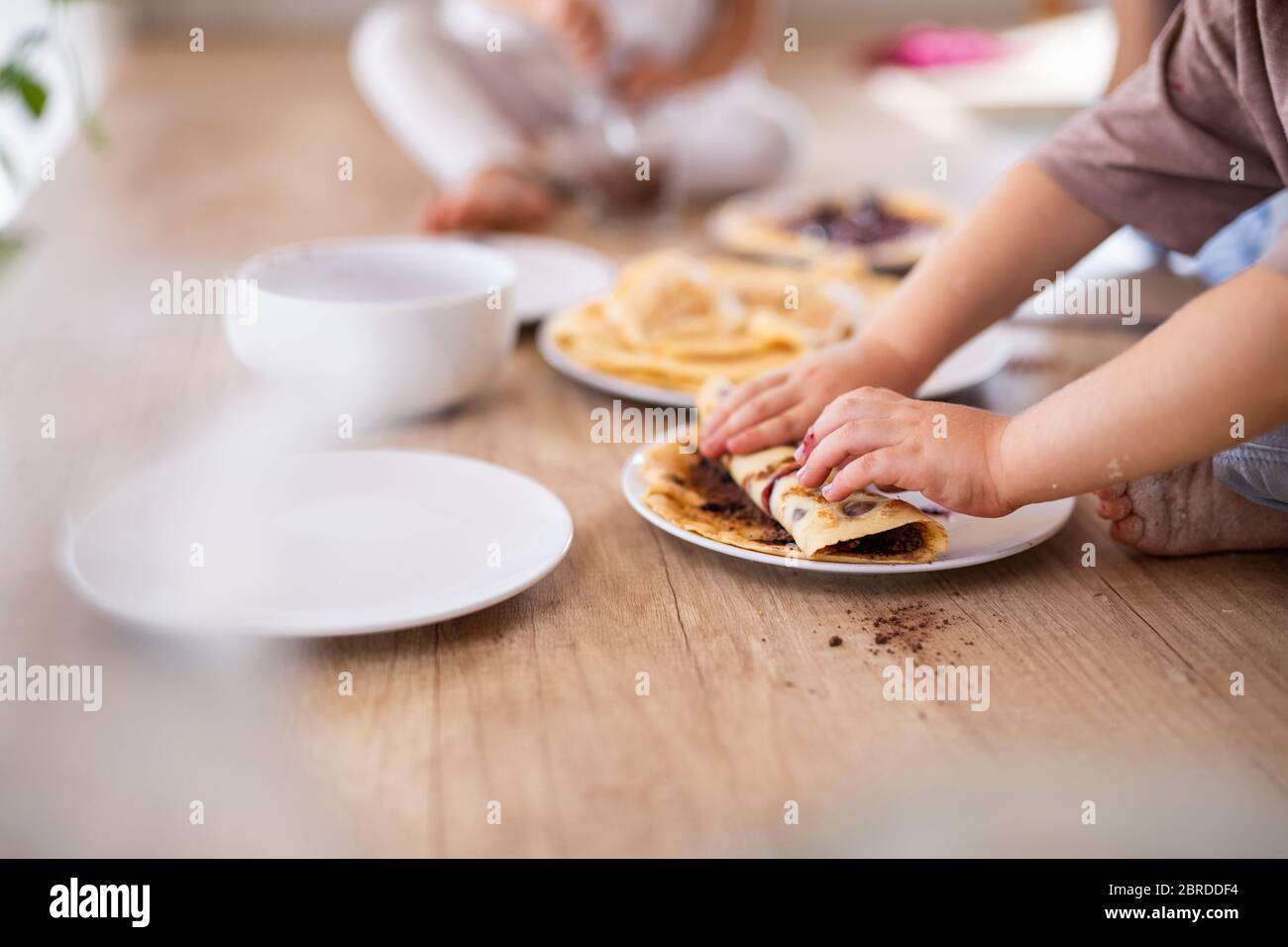 Unkenntlich zwei kleine Kinder drinnen in der Küche essen Pfannkuchen. Stockfoto