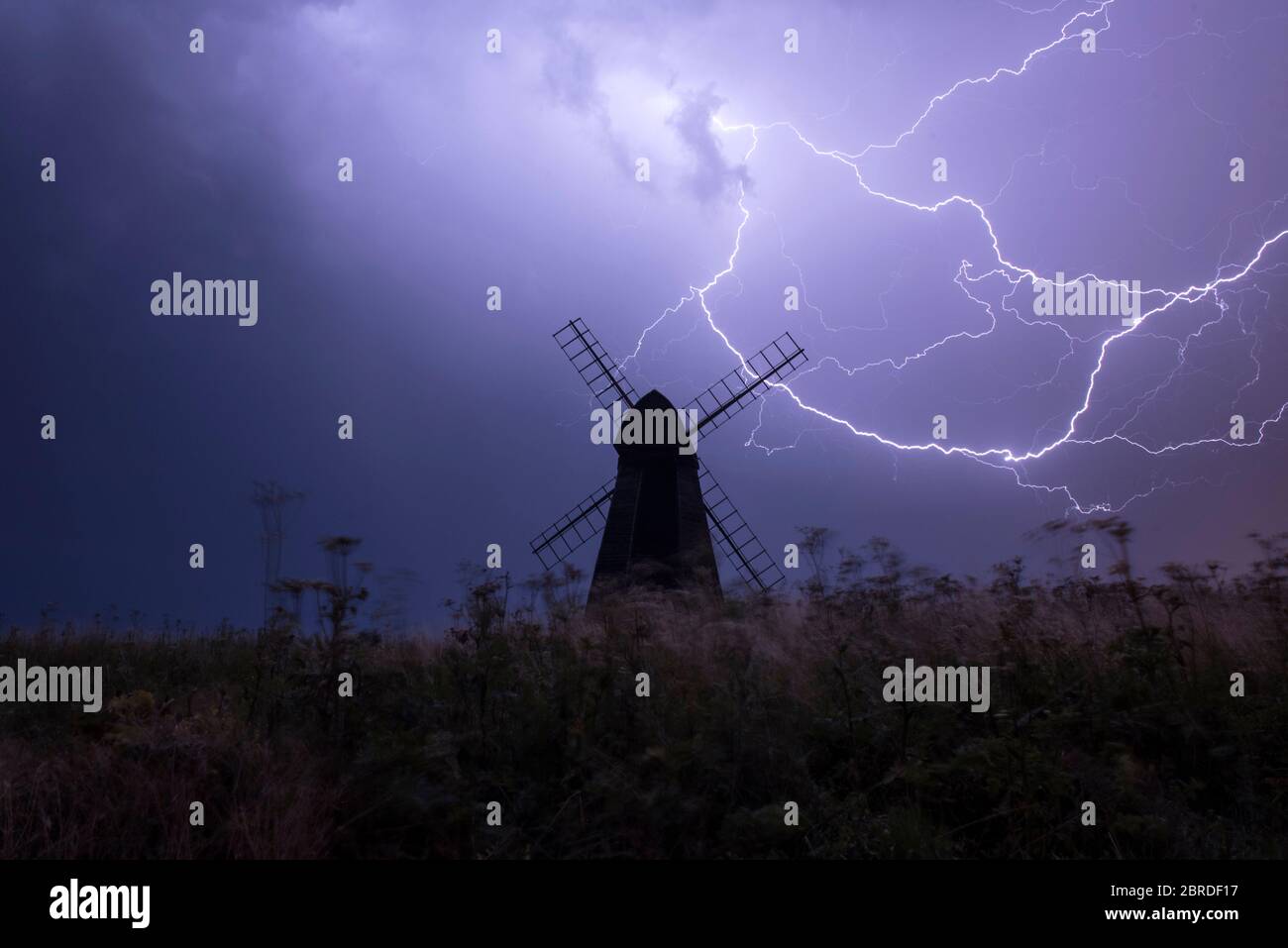 Gabelblitze schlagen in der Nacht ein Sommersturm hinter Beacon Mill, einer alten Schuttenwindmühle in Rottingdean, East Sussex Stockfoto