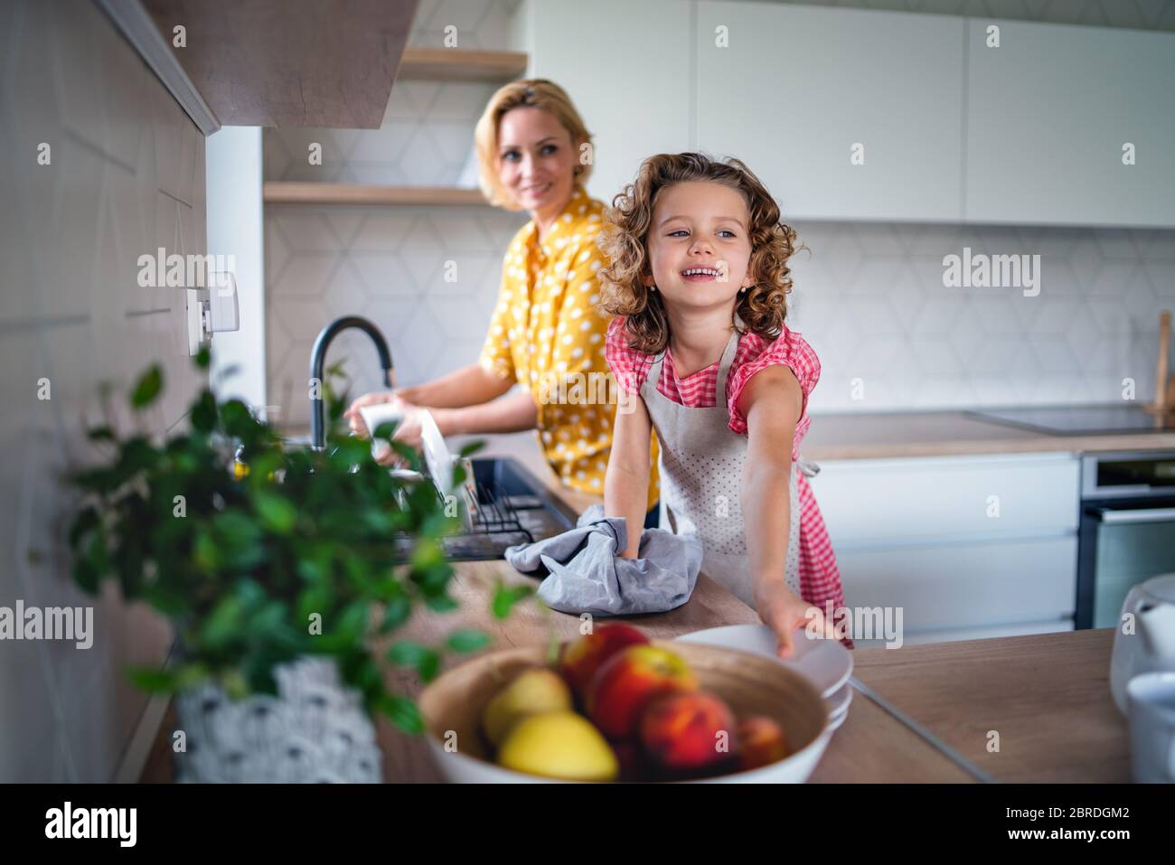 Ein nettes kleines Mädchen mit Mutter drinnen in der Küche zu Hause, Geschirr abwaschen. Stockfoto