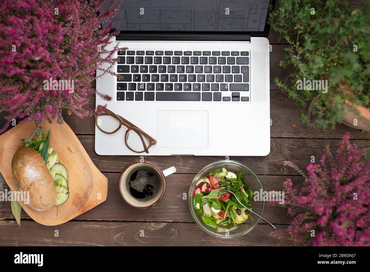 Zusammensetzung von Laptop und Mittagessen auf Bank im Freien auf der Terrasse. Stockfoto