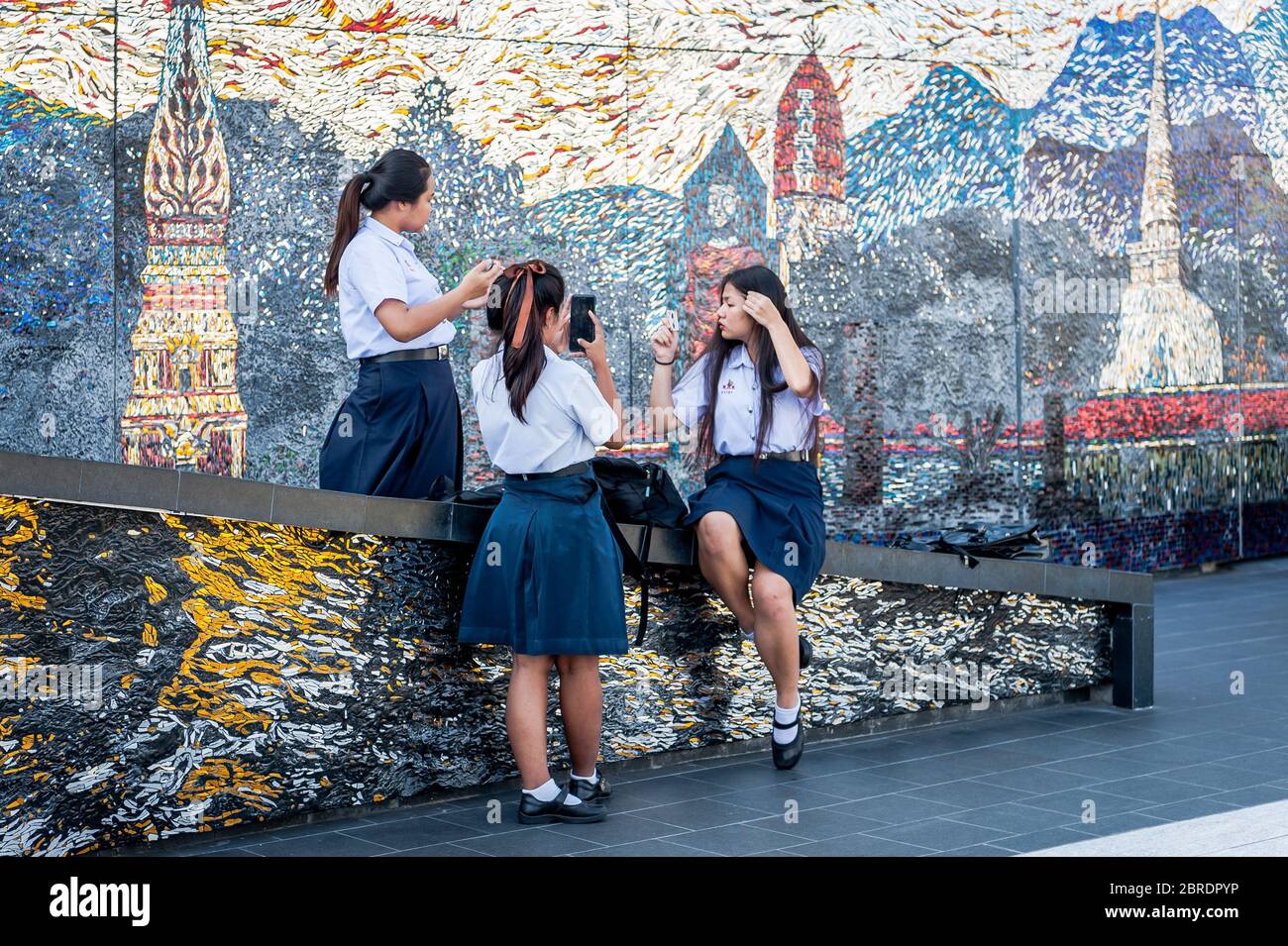 Eine Gruppe thailändischer Universitätsstudenten nimmt sich einen Moment Zeit, um Make-up zu machen, zu plaudern und Telefone auf dem Balkon der Iconsiam Shopping Mall, Bangkok, zu betrachten. Stockfoto