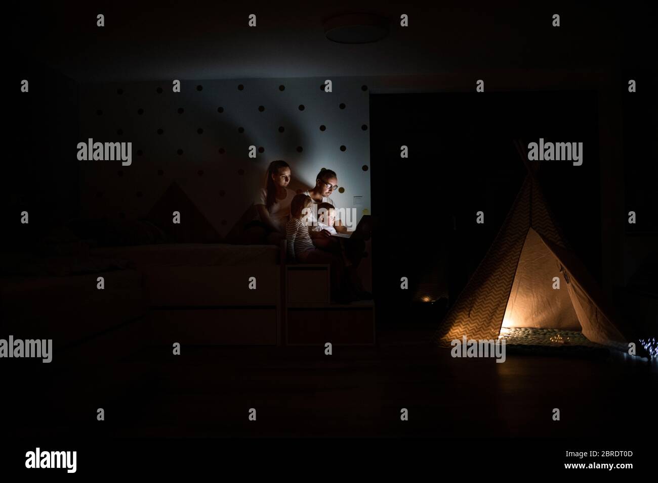 Familie mit Kindern, die im Schlafzimmer sitzen und einen Laptop benutzen. Stockfoto