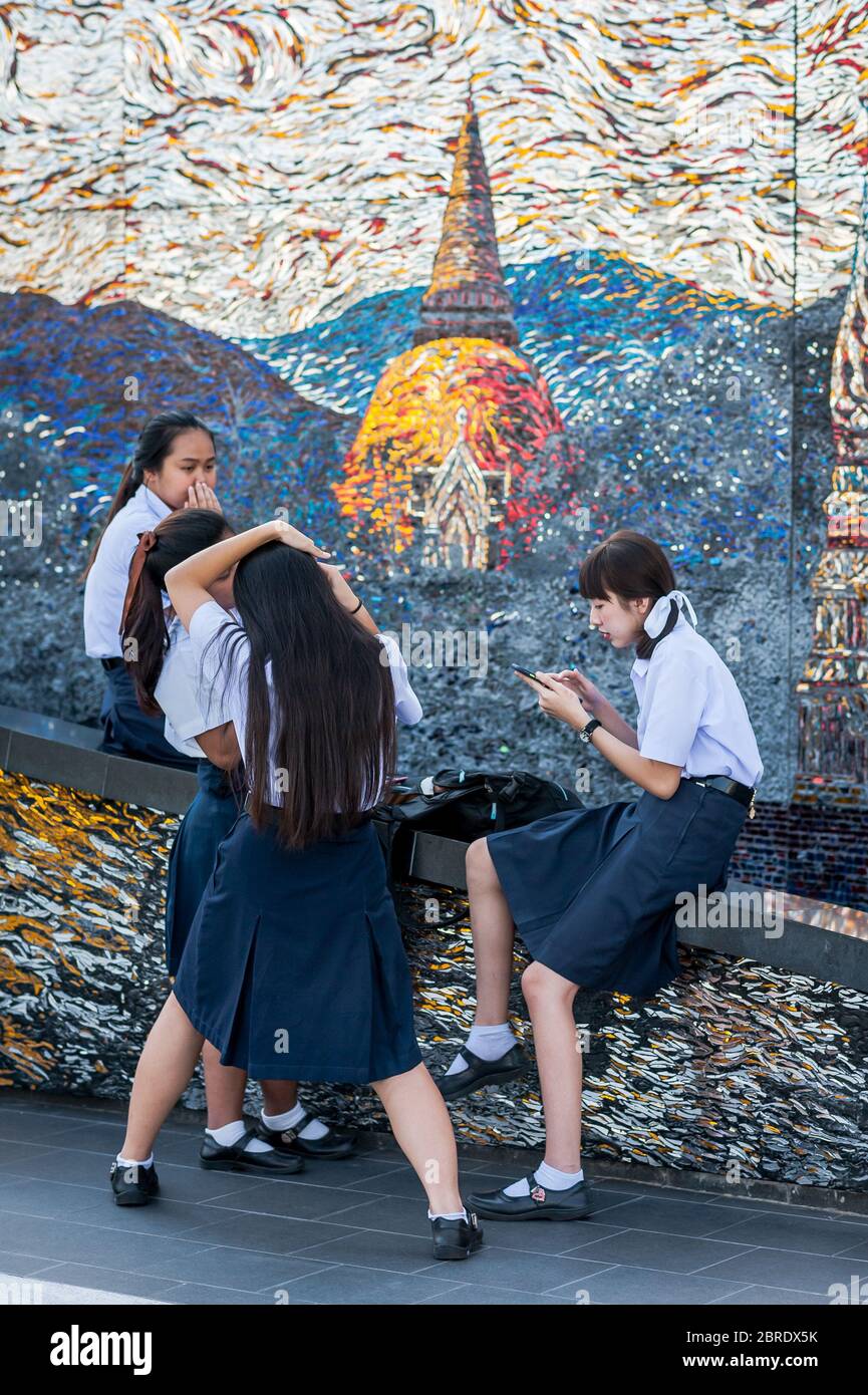 Eine Gruppe thailändischer Universitätsstudenten nimmt sich einen Moment Zeit, um Make-up zu machen, zu plaudern und Telefone auf dem Balkon der Iconsiam Shopping Mall, Bangkok, zu betrachten. Stockfoto