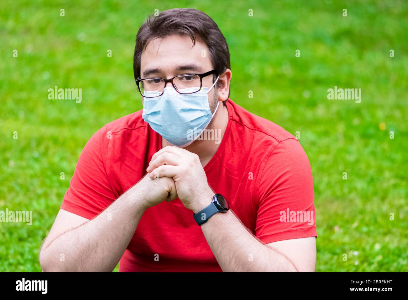 Fetter Mann mit Gesichtsmaske auf dem Gras sitzend Stockfoto