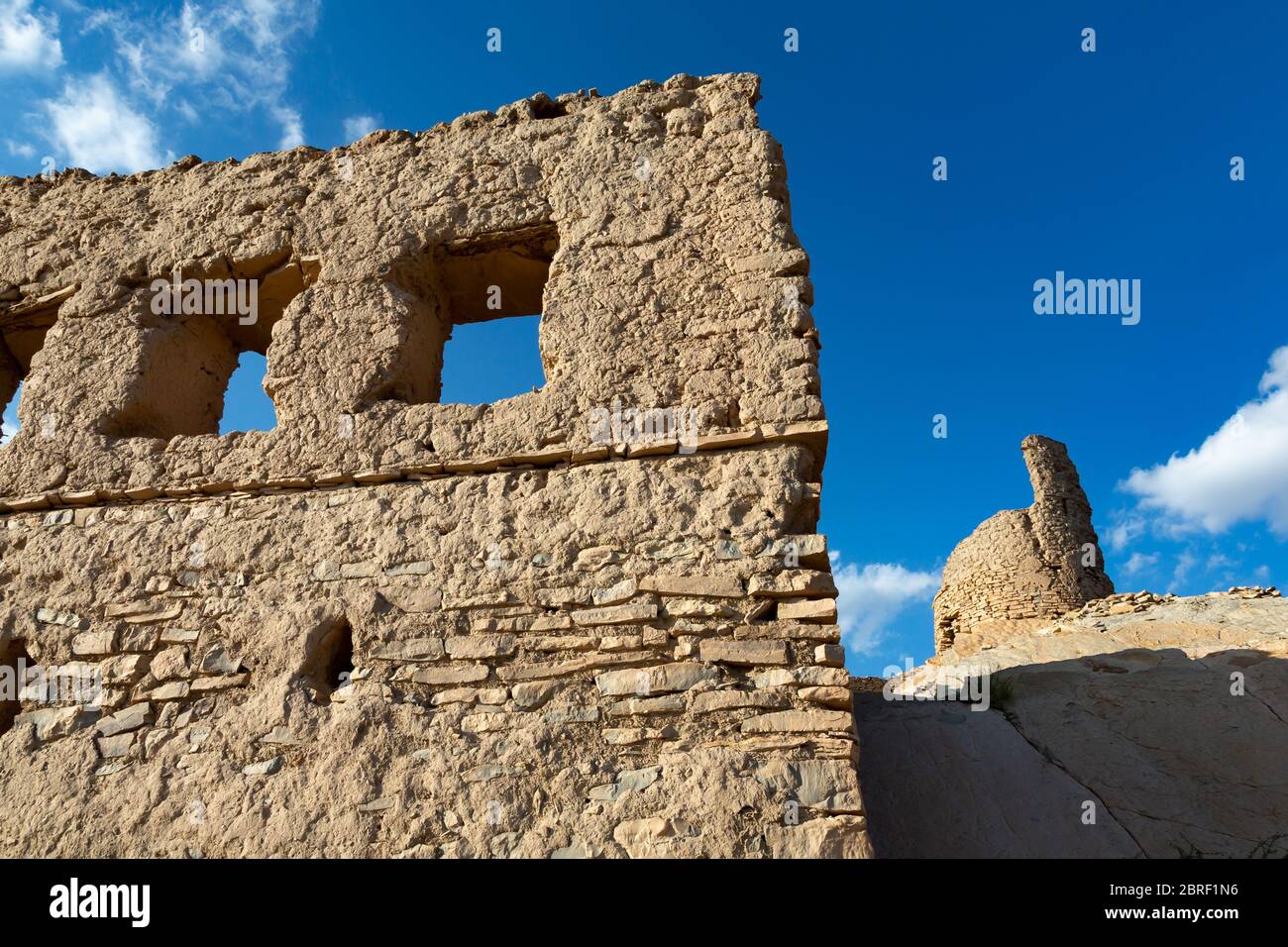 Verbleibende Ruinenmauer in Birkat al Mawz, Oman, mit Ruinenturm im Hintergrund Stockfoto