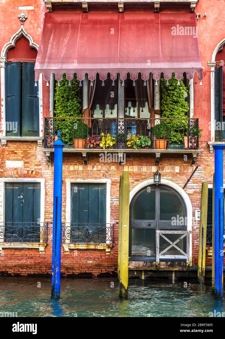 Alte rote Fassade in Venedig, Italien. Vorderansicht des Gebäudes mit Eingang in Venedig. Vintage Hotel oder Wohnhaus am Wasser. Alt Stockfoto