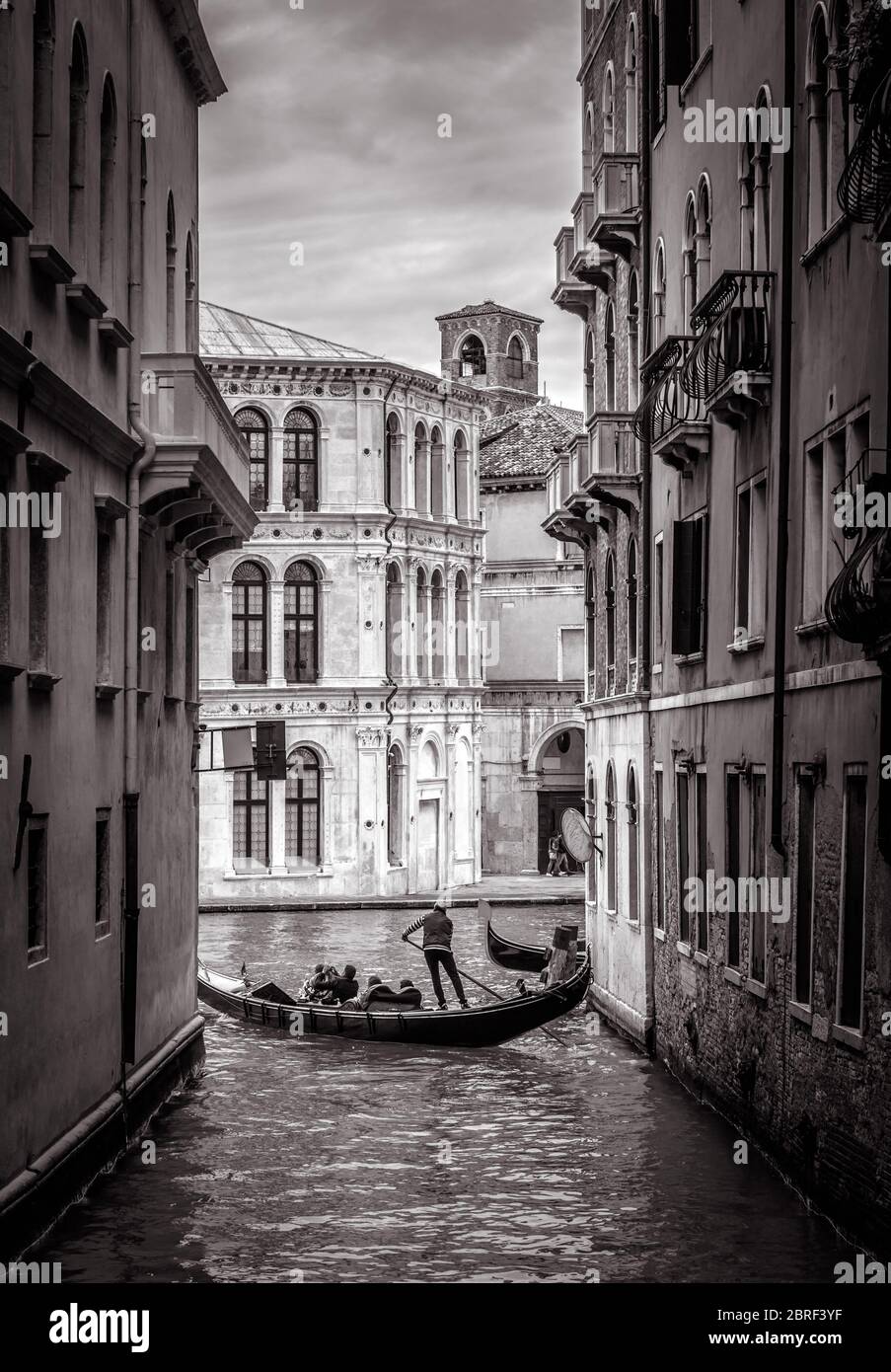 Venedig in schwarz-weiß, Italien. Alte schmale Straße mit einiger Gondel in der Ferne. Romantische Wassertour über die alten Kanäle Venedigs. Konzept der tr Stockfoto