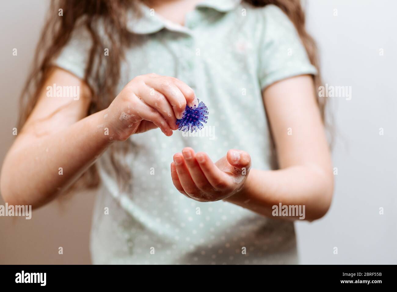 Mädchen mit Händen in Seife hält ein abstraktes Modell des Coronavirus. Coronavirus COVID-19 Ausbruch Infektion Prävention und Kontrolle. Hygiene- und Gesundheitskonzept Stockfoto