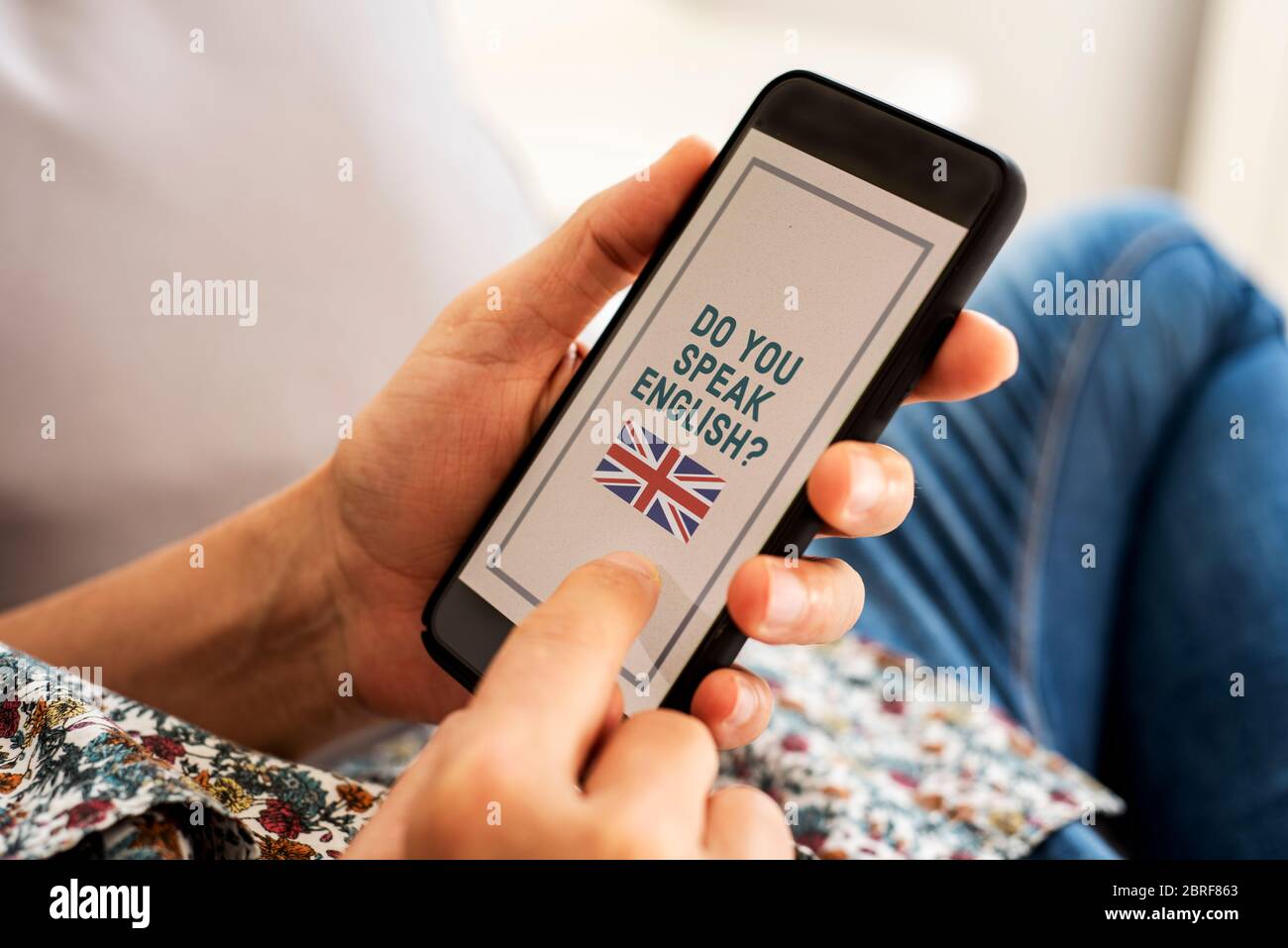 Nahaufnahme eines jungen kaukasischen Mannes, der lässige Kleidung trägt, drinnen auf einer Couch sitzt, sein Smartphone in den Händen hat mit dem Text do you speak en Stockfoto