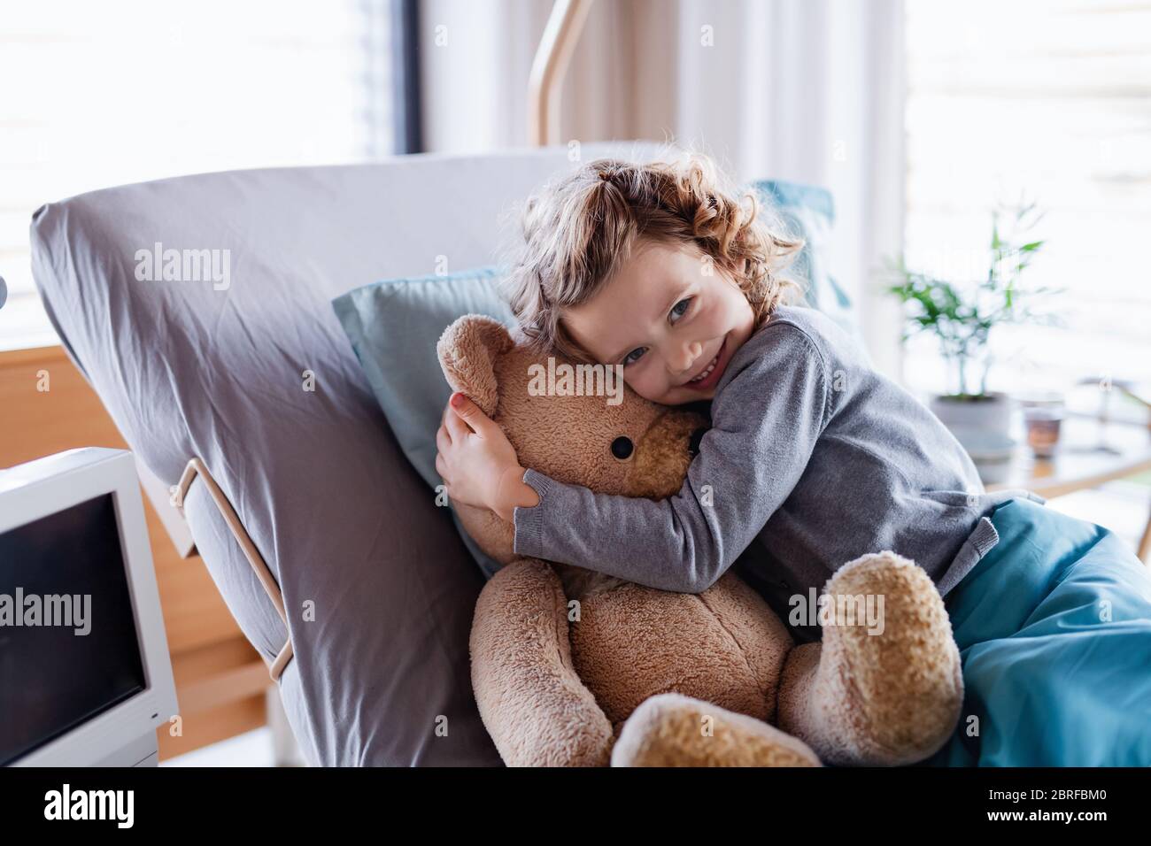 Lächelndes kleines Mädchen mit Teddybär im Bett im Krankenhaus. Stockfoto