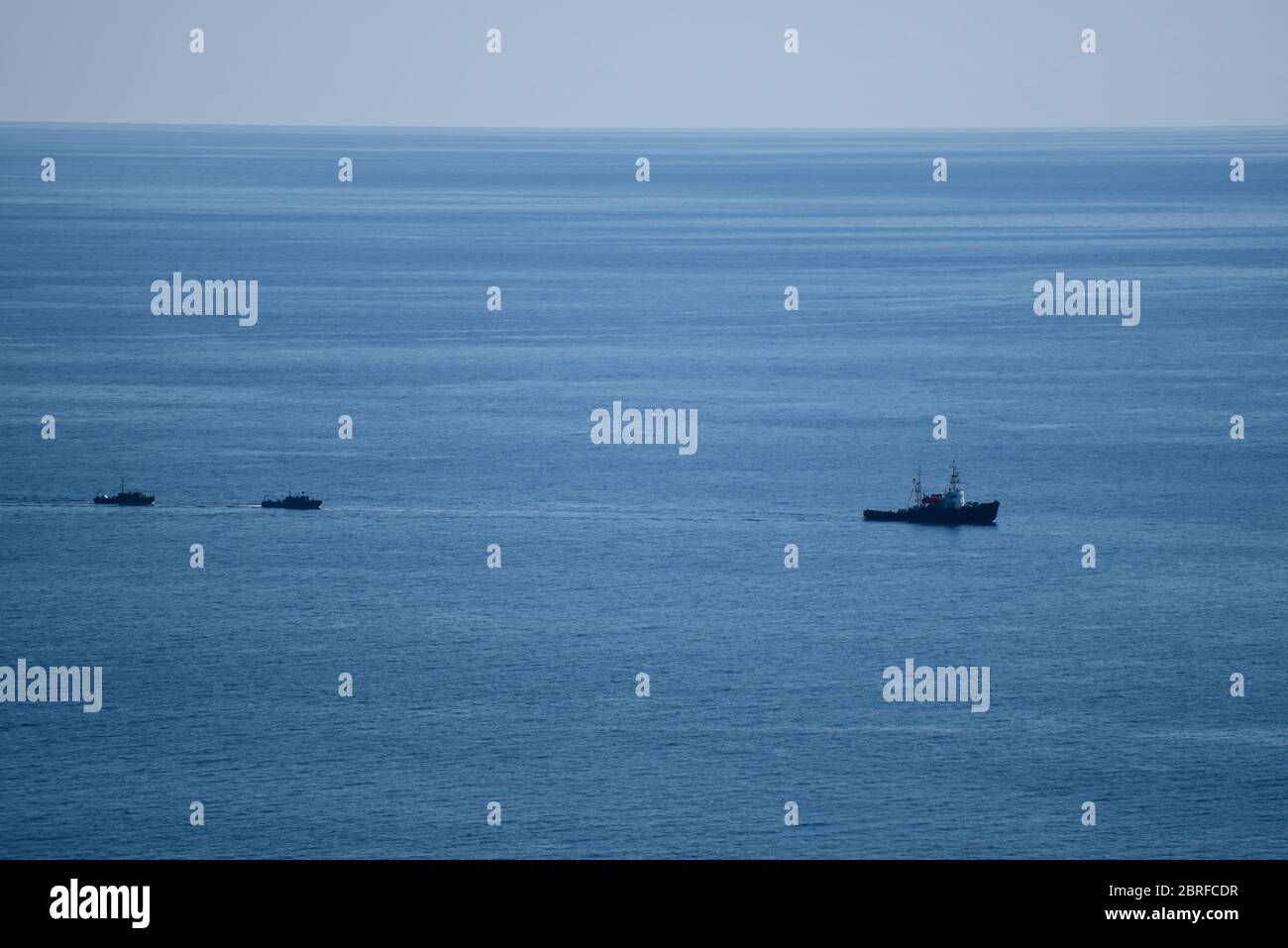 Ein großes Seeschiff segelt, und zwei kleine Schiffe segeln hinter ihm, in einem ruhigen blauen Meer. Stockfoto