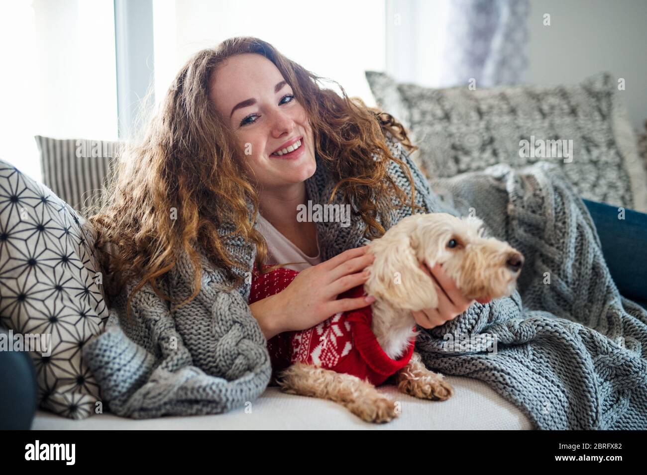 Junge Frau, die sich zuhause auf dem Sofa mit Haustier Hund entspannt. Stockfoto