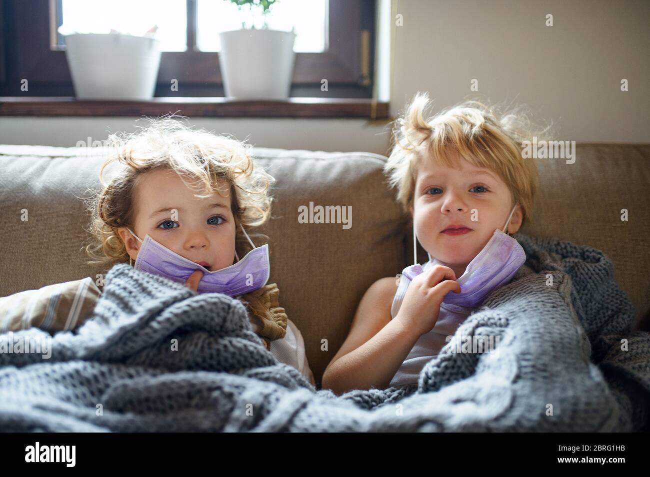 Zwei kleine kranke Kinder mit Gesichtsmaske zu Hause im Bett liegend. Stockfoto