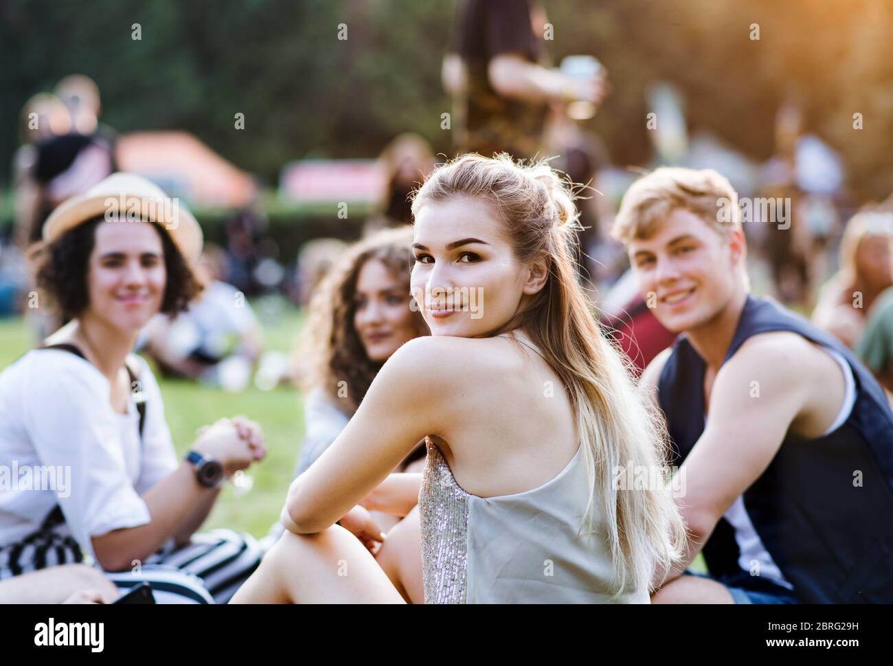 Gruppe junger Freunde, die auf dem Boden beim Sommerfest sitzen. Stockfoto