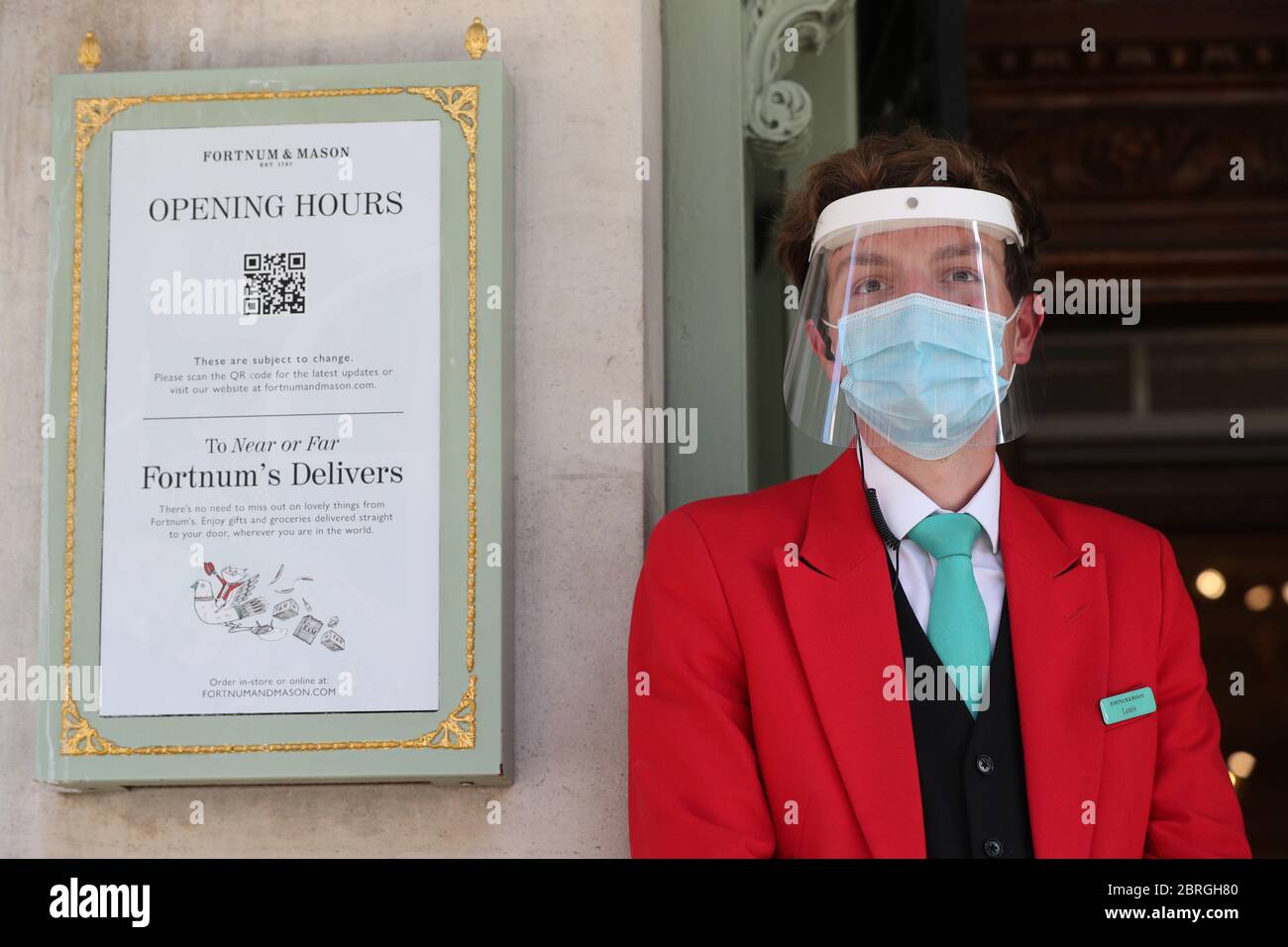 Ein uniformierter Türsteher trägt eine Maske und ein Visier vor dem Eingang des Kaufhauses Fortnum & Mason in Piccadilly, im Zentrum Londons, das seit heute zwei Food Halls für Kunden eröffnet hat, da die Beschränkungen für die Sperrung des Coronavirus gelockert werden. Stockfoto