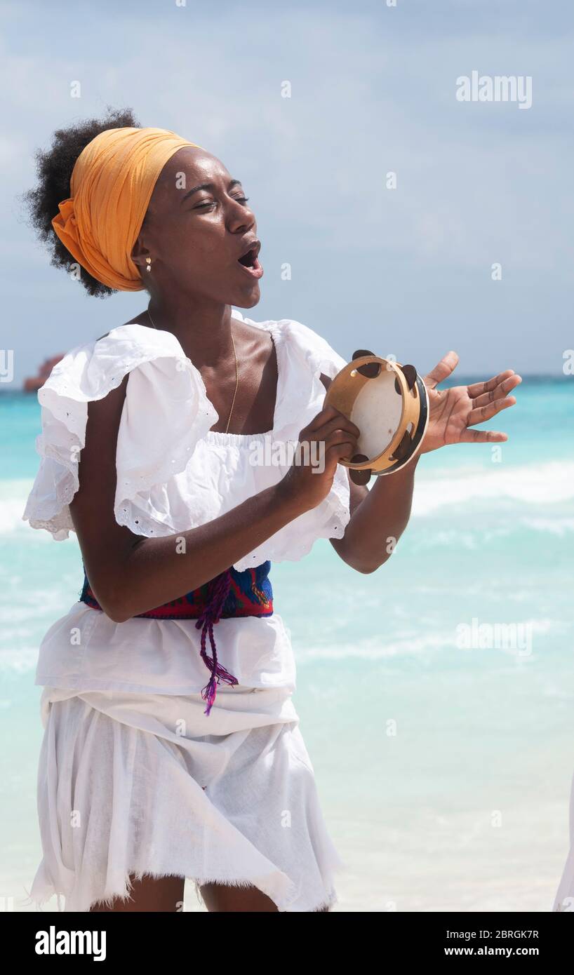 Junge Frau, die am Strand tanzt und Tamburin spielt. Im Hintergrund das Karibische Meer, Mexiko Stockfoto