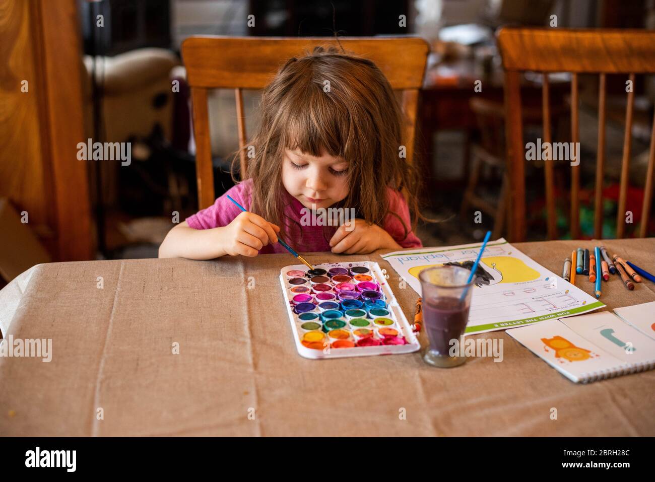 Ein 5-jähriges Mädchen malt mit einer Vielzahl von Aquarellfarben. Stockfoto