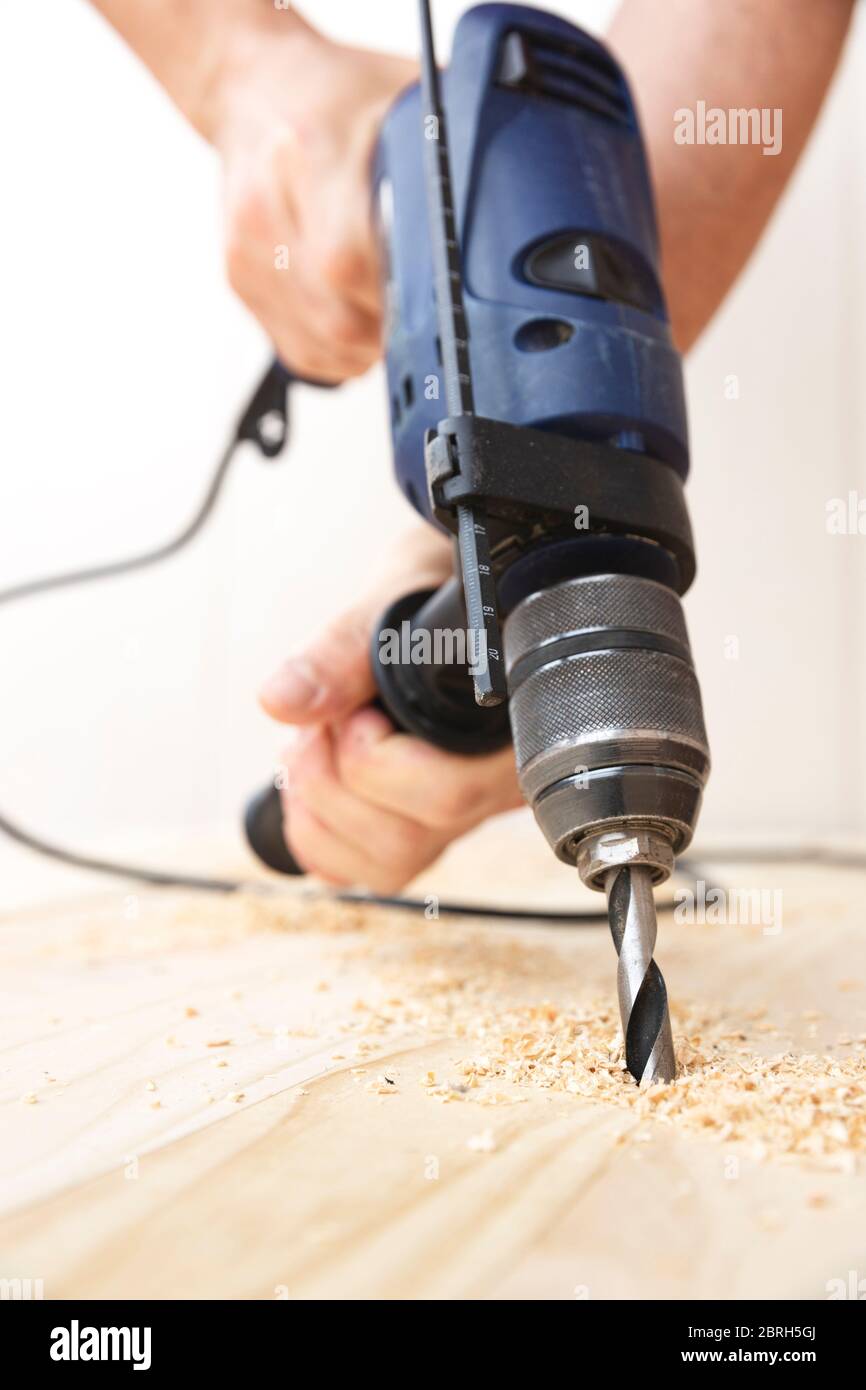 Detail der Hände einer Person Bohren eines natürlichen Kiefernholzbretts mit einem Bohrer. Arbeits- und DIY-Konzept. Stockfoto