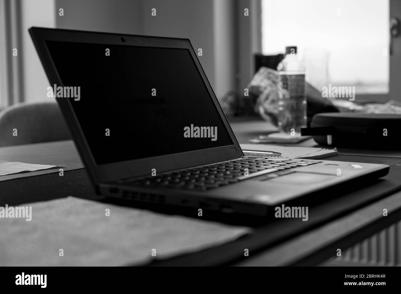 Ein Schwarz-Weiß-Foto eines abgesetzten Laptops, das in einer realistischen Wohnumgebung auf einem Küchentisch platziert ist und das Konzept des Arbeitens von zu Hause aus zeigt Stockfoto