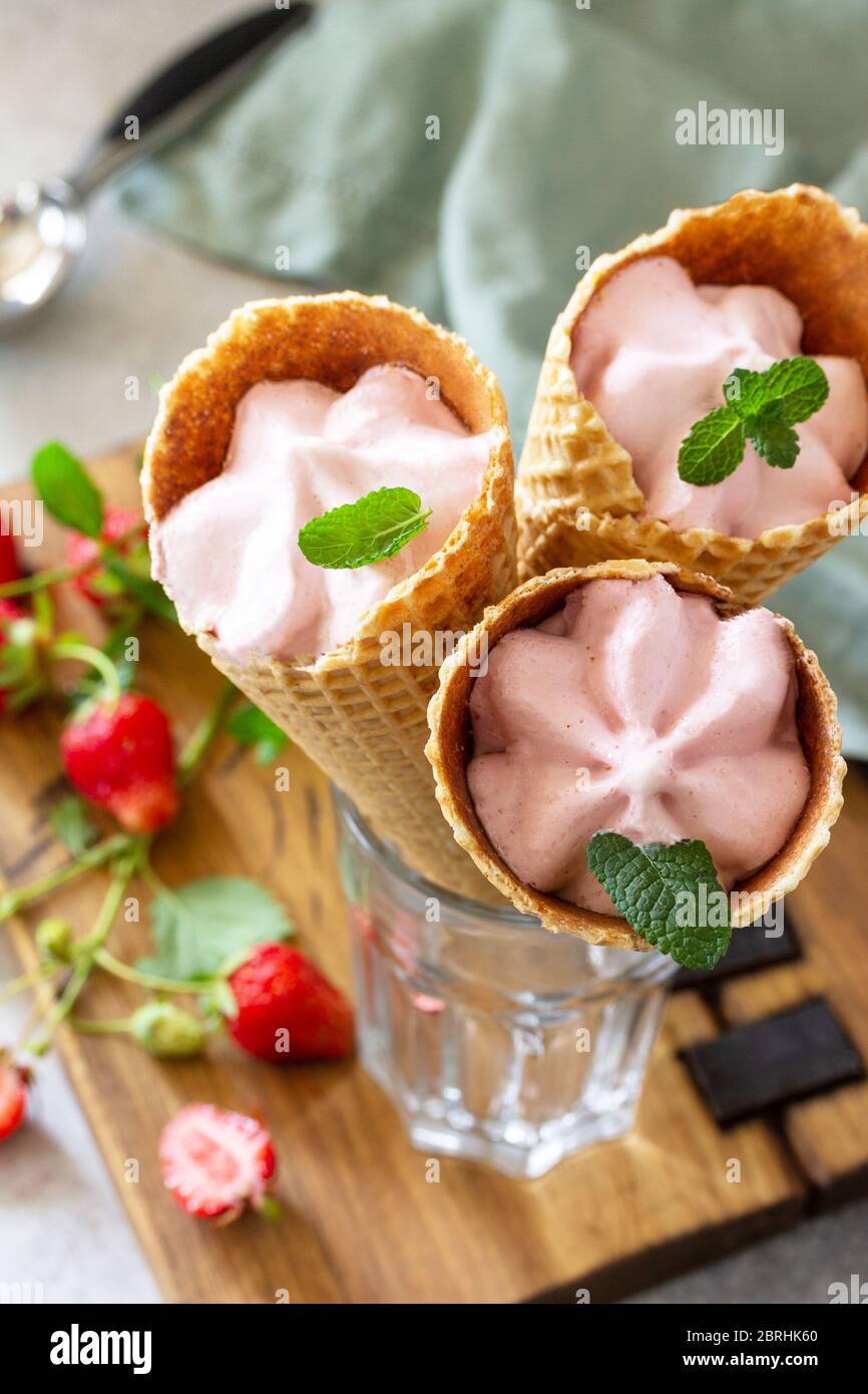 Hausgemachte Bio-Erdbeer-Eiscreme. Erdbeere von Eis in Waffelzapfen auf einem hellen Stein oder Schiefer Tisch. Stockfoto