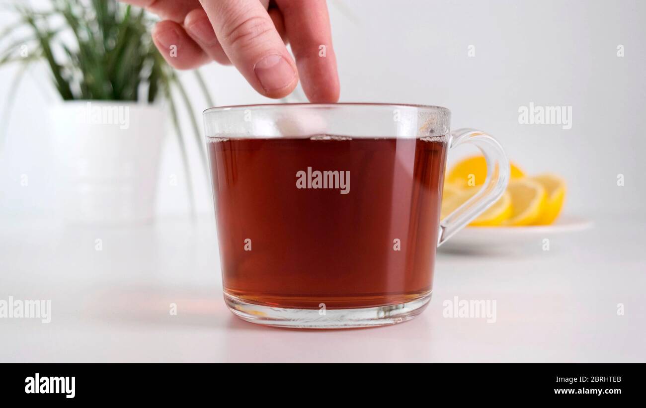 Zuckerwürfel in eine Tasse heißen Tee geben. Nahaufnahme. Stockfoto