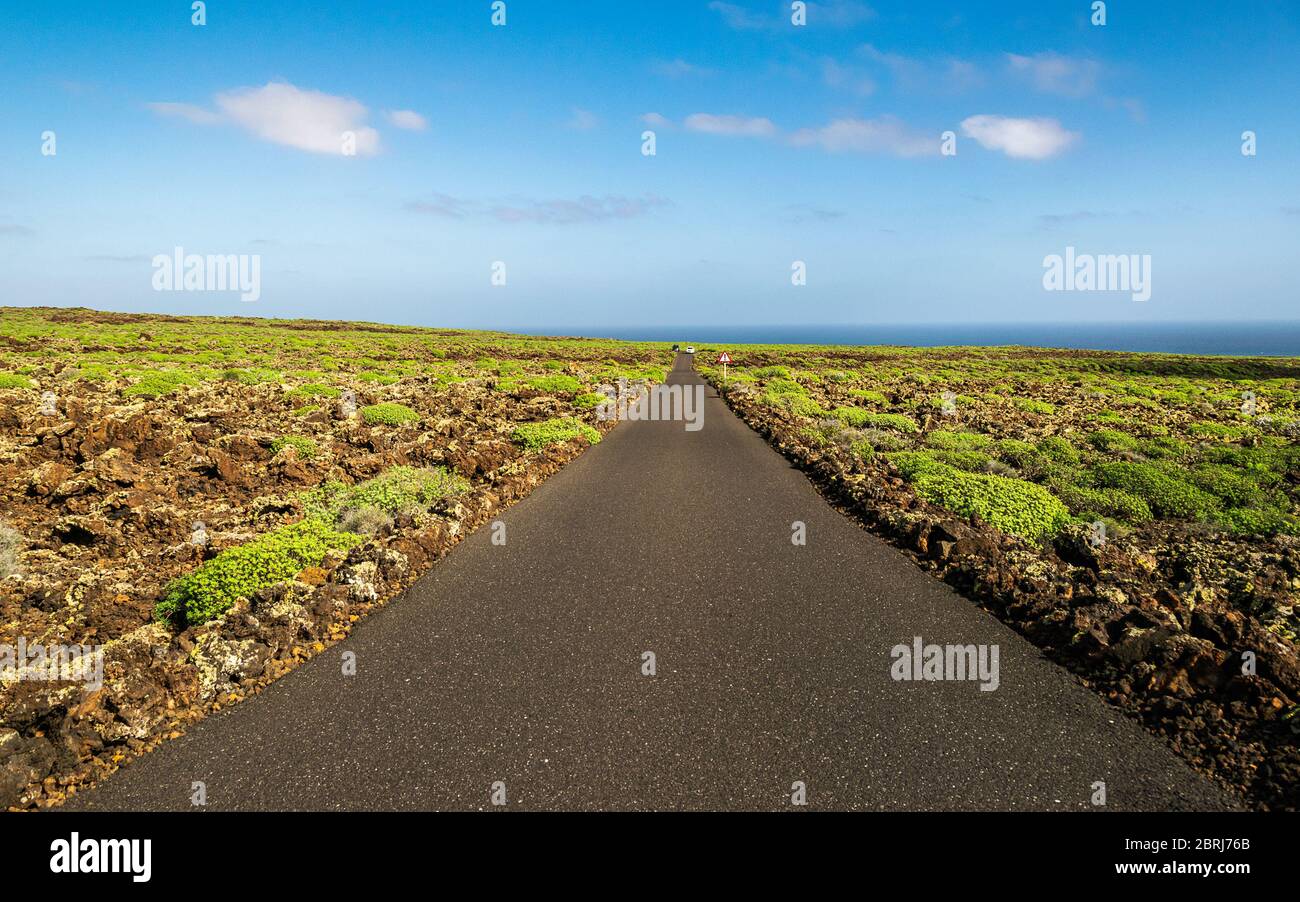 Auf Lanzarote führt eine gerade Asphaltstraße in Richtung Meer. Schöne vulkanische Landschaft von Lanzarote, Kanarische Inseln, Spanien. Stockfoto