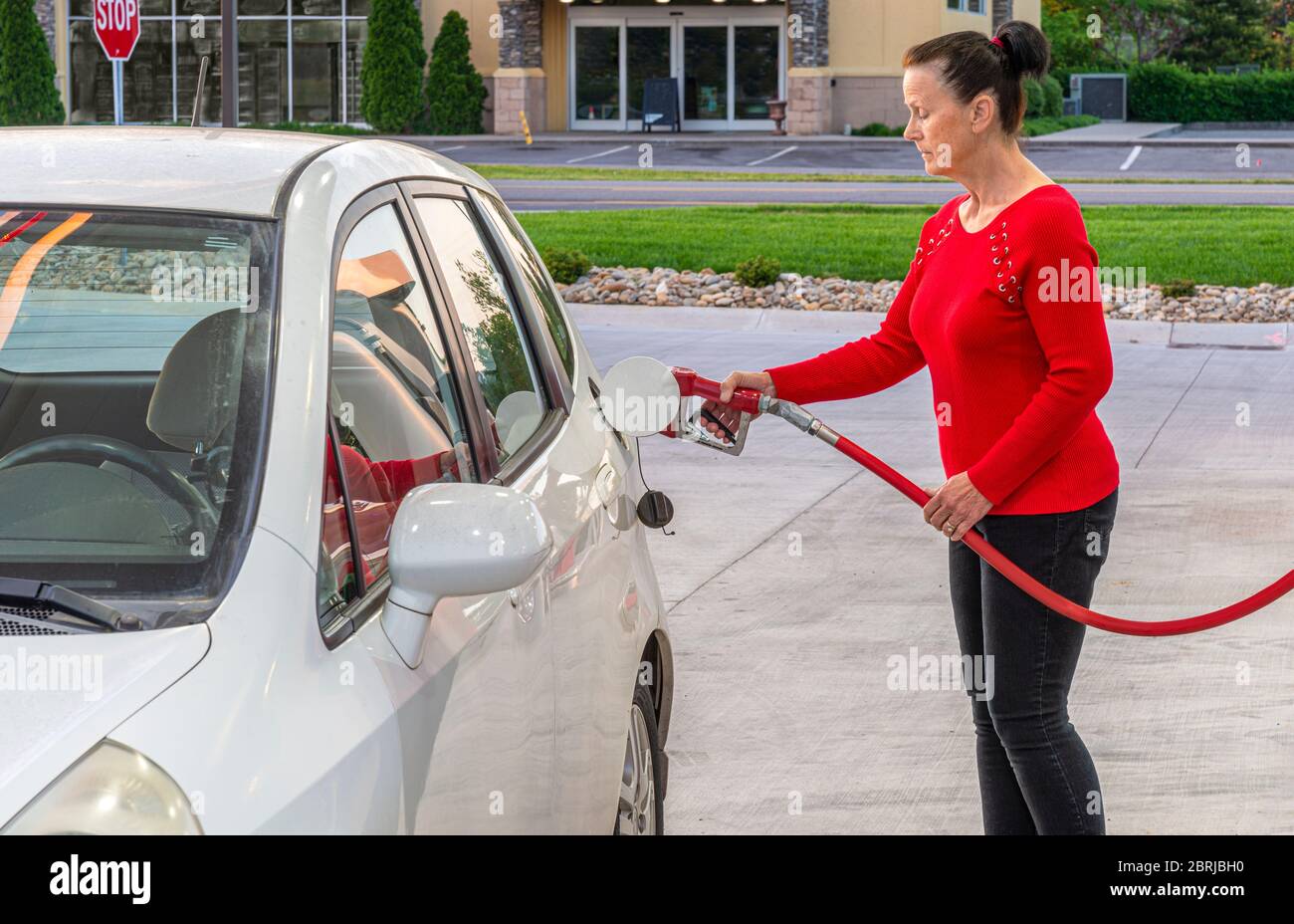 Horizontale Aufnahme einer Frau mittleren Alters, die Gas in ihr weißes Auto pumpt. Stockfoto