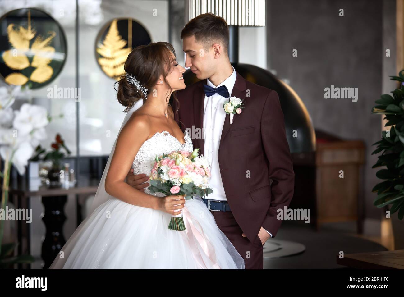 Schöne Braut in einem weißen Kleid und ein schöner Bräutigam in einem Burgund Anzug schauen sich gegenseitig an. Stockfoto