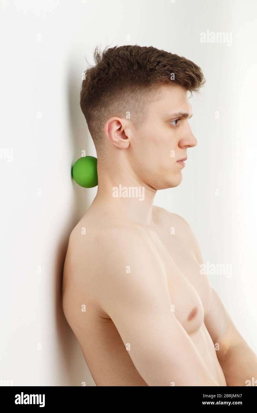Schöner Mann zeigt Übungen mit Wand und Ball für eine myofascial Release Massage von Triggerpunkten. Massage des Nackenmuskels. Stockfoto
