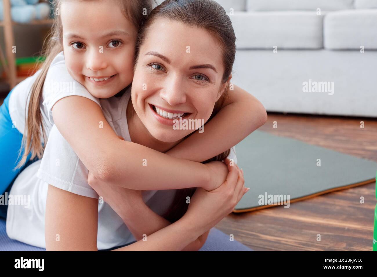 Junge Erwachsene Frau und ihre kleine Tochter machen gemeinsam Sporttraining zu Hause Stockfoto
