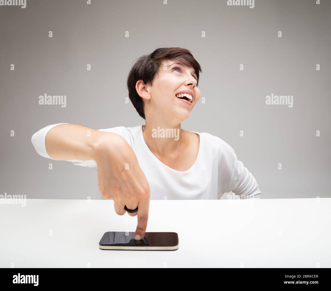 Eine selbstgefällig Frau, die auf ihr Mobiltelefon zeigt, während sie mit einem erbarmungsvollen selbstgerechten Ausdruck in die Luft blickt Stockfoto