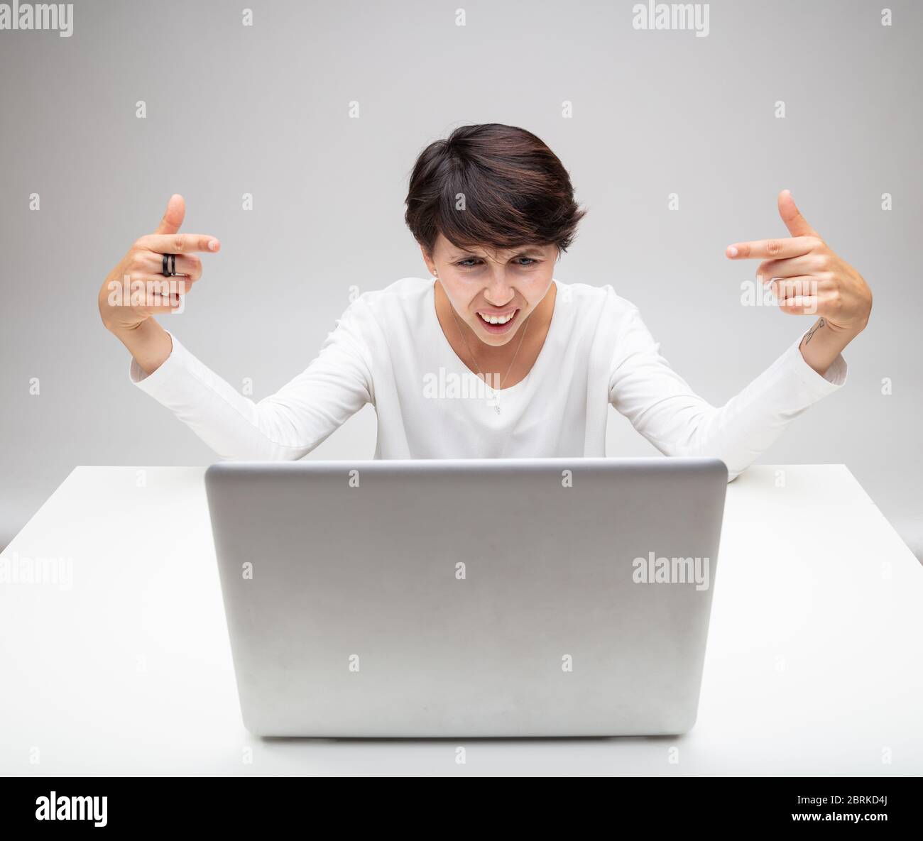 Verwirrt starrte Frau ungläubig auf ihren Laptop mit einem Grimassen und einem intensiven Blick, während sie mit ihren Fingern auf den Bildschirm über einem Grau zeigt Stockfoto