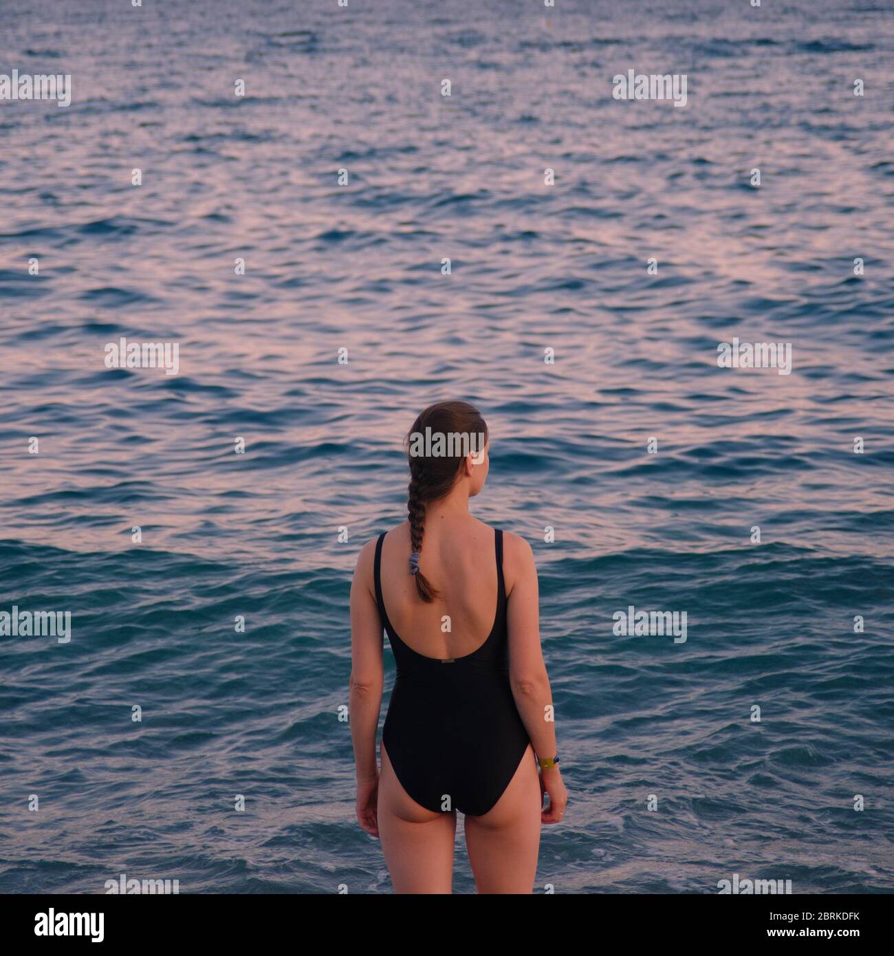 Mädchen in einem schwarzen Badeanzug mit dem Rücken zum Meer Stockfoto