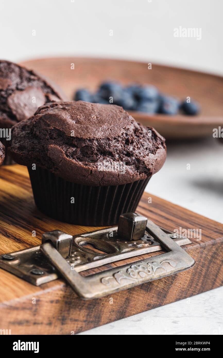 Leckere hausgemachte Schokoladenmuffins auf rustikalem Holzbrett, frische Sommerbluebeeren in Keramikplatte Stockfoto