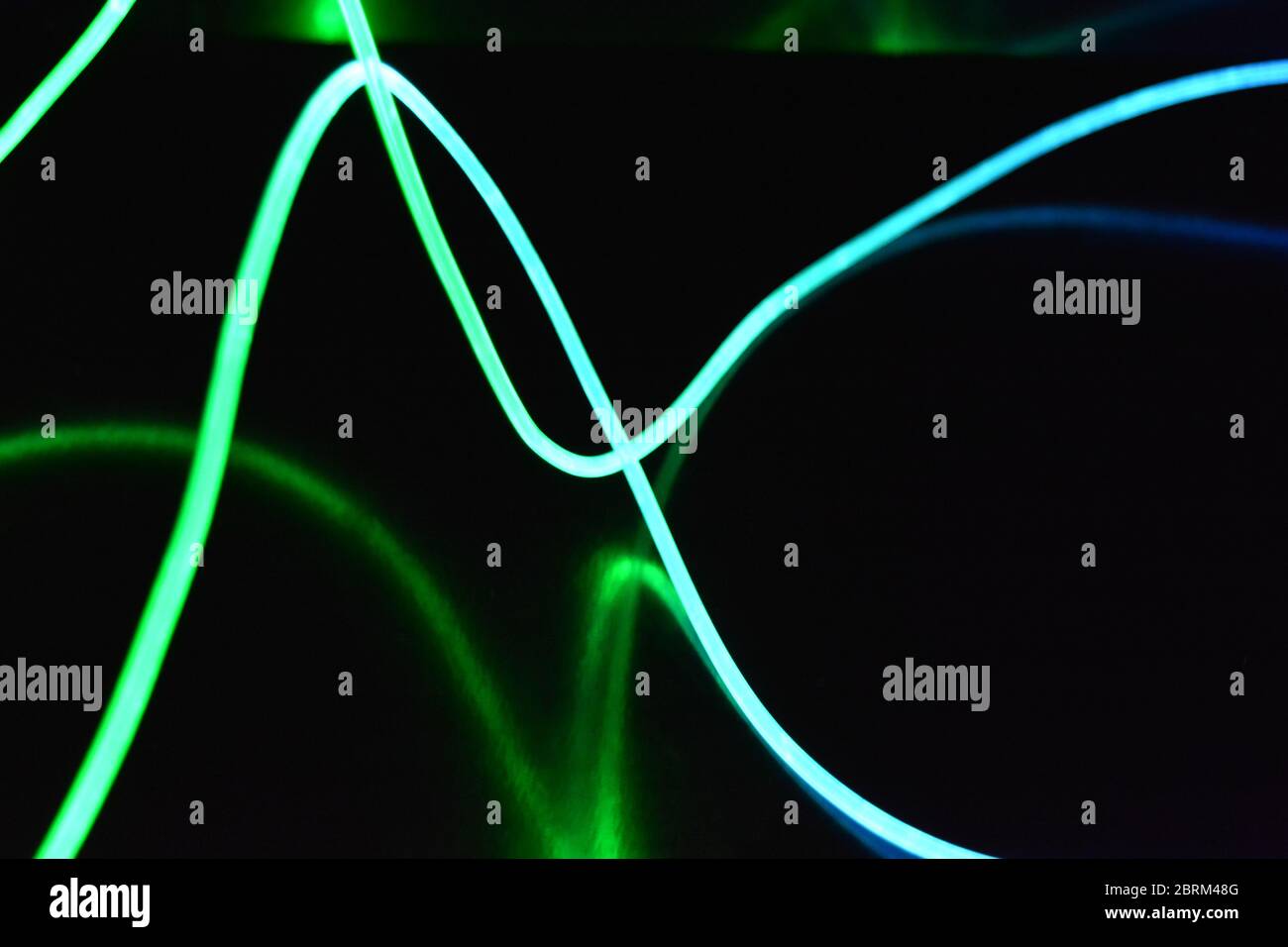 Grüner und blauer Lichtleiter, ein Lichtleiterkabel mit unterschiedlicher Lichtübertragung, Lichtspektrum und Lichteffekten, das sich in einem chaotischen Zustand befindet. Stockfoto