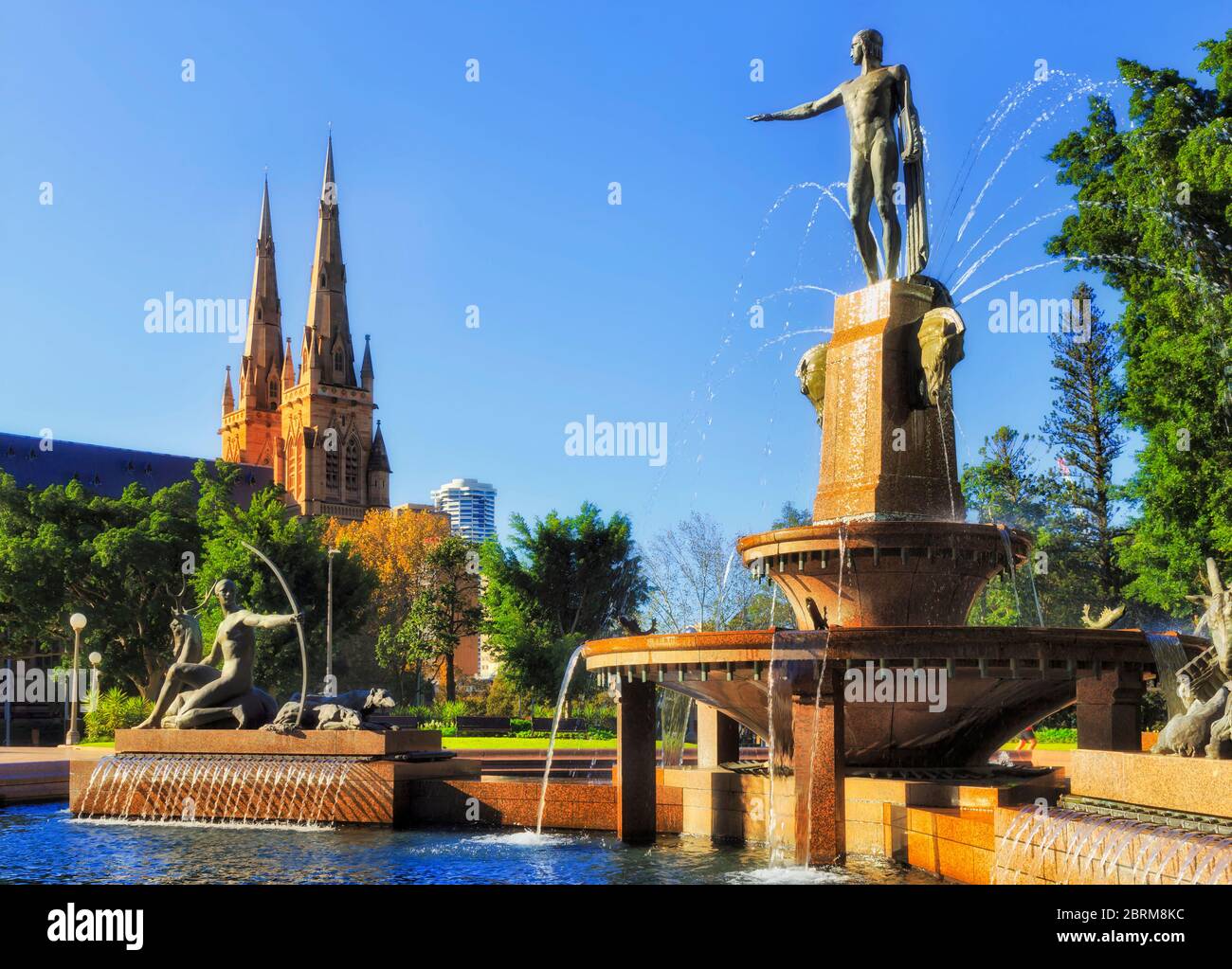 Türme und Türme der gotischen Kathedrale in Sydney nahe dem Hyde Park und erfrischender Wasserbrunnen an einem sonnigen Tag. Stockfoto