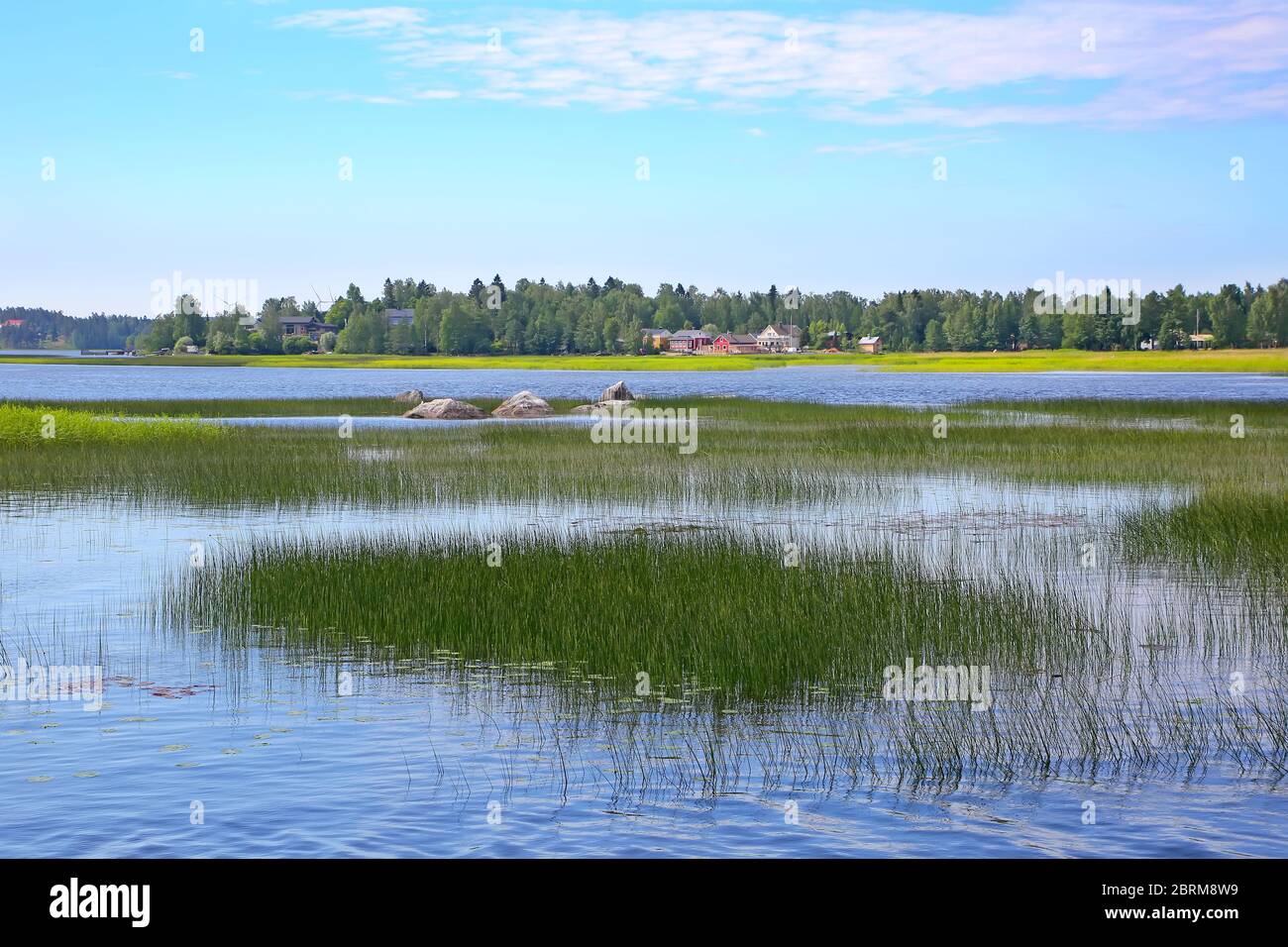 Schöne Landschaft mit Schilf im Wasser & Dörfchenam Flussufer des Kymi Flusses, in der Nähe von Kotka, Finnland. Stockfoto