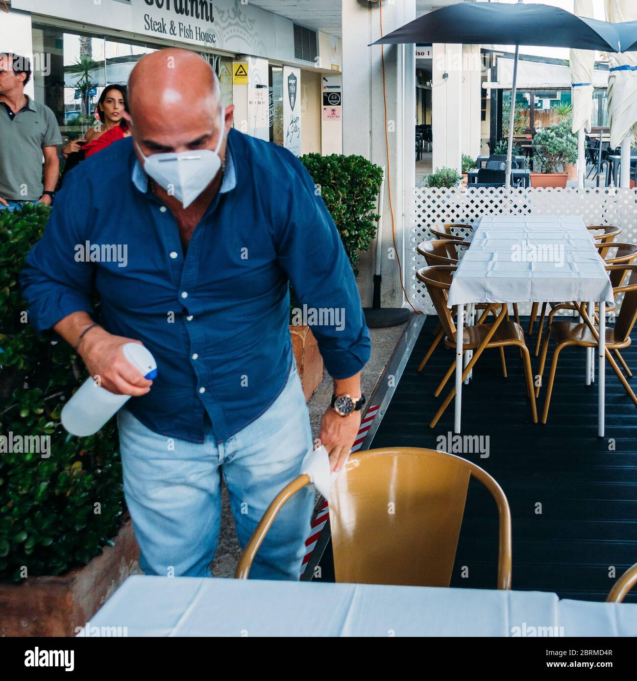 Mann mit einer Gesichtsmaske reinigt einen Tisch im Restaurant, um die Ausbreitung des Covid-19 Virus zu reduzieren Stockfoto