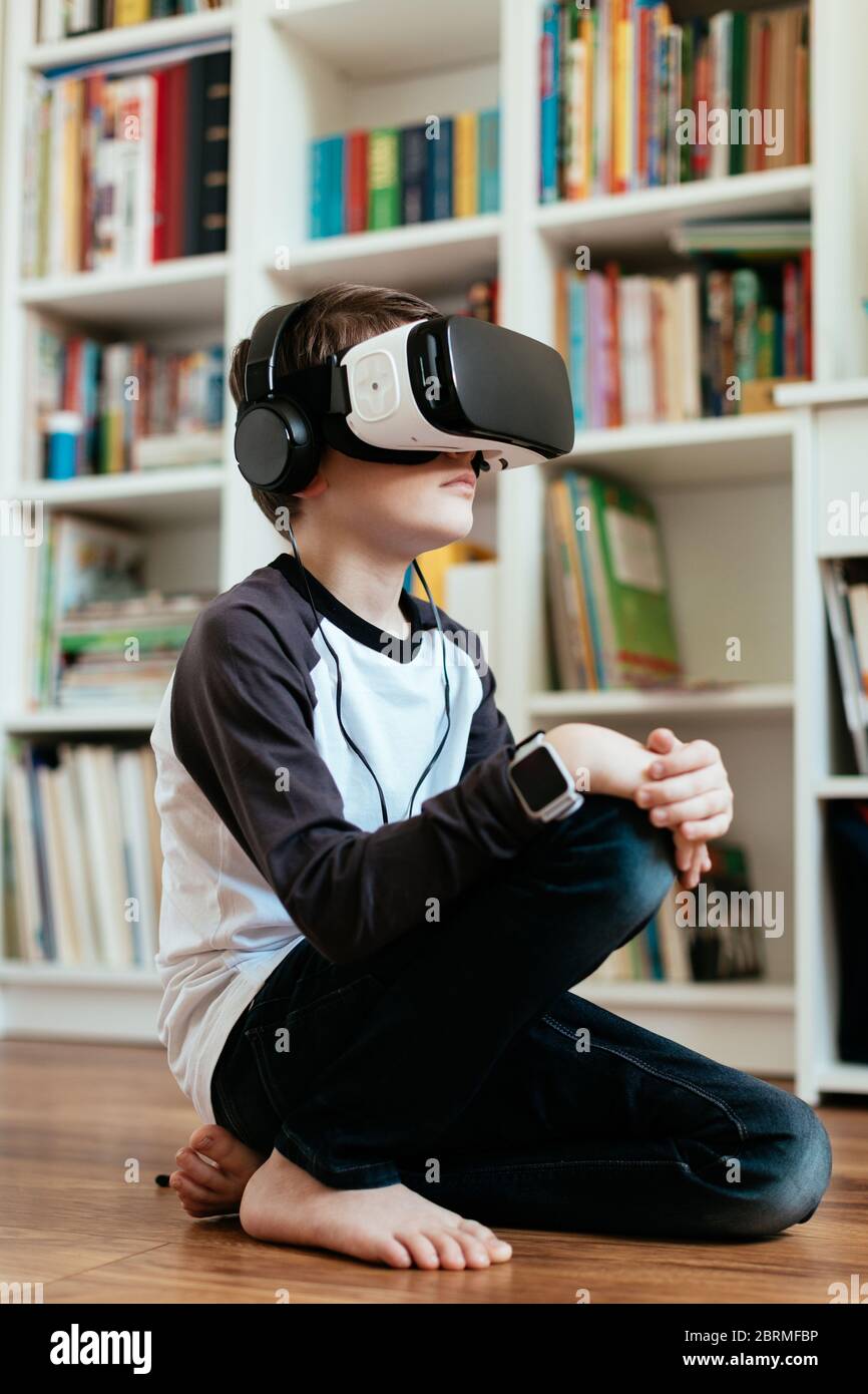 Junge sitzt auf dem Boden mit VR-Brille. Teenager mit Virtual Reality-Headset und Kopfhörern. Stockfoto
