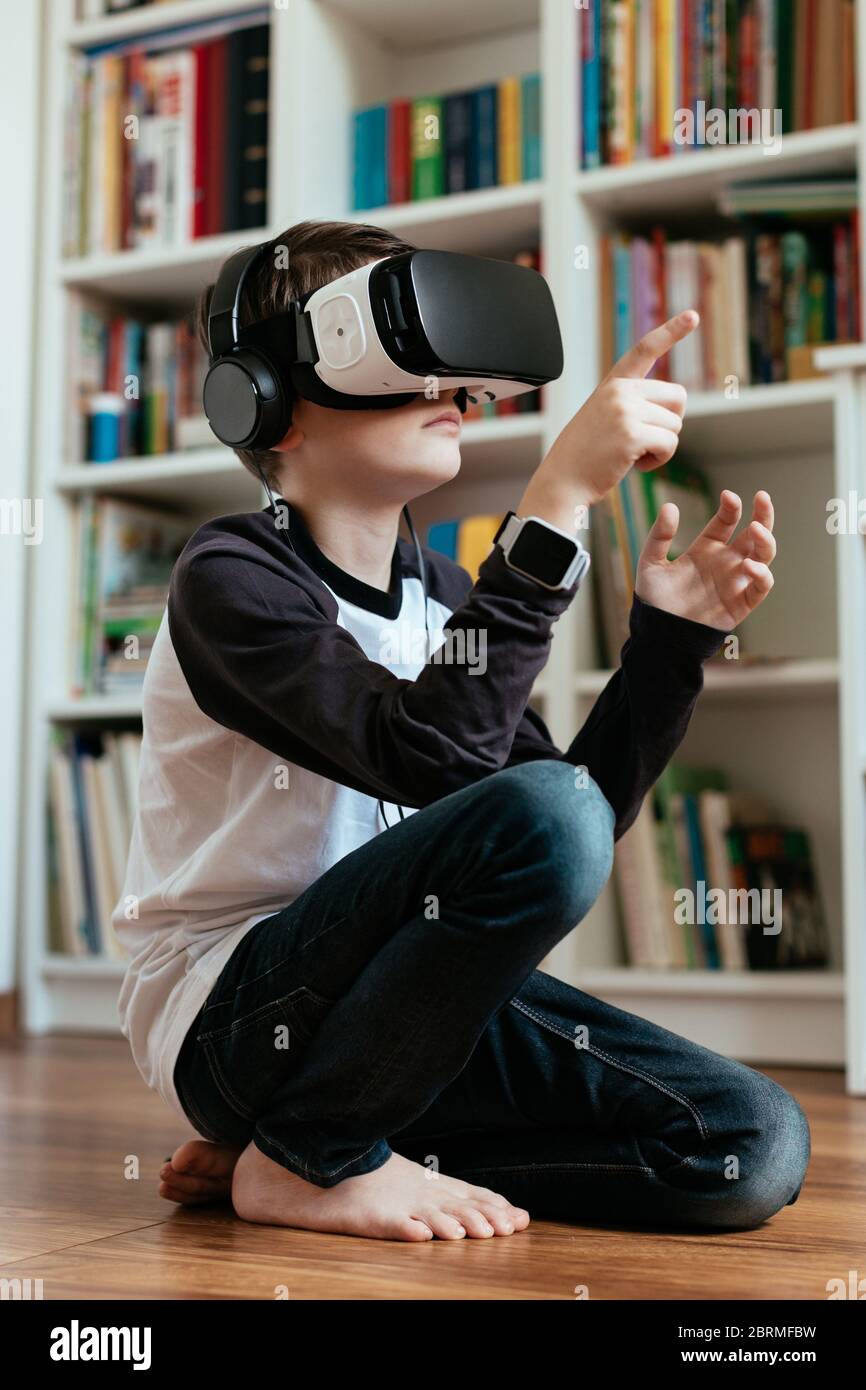 Teenager, der auf dem Boden sitzt und VR-Headset trägt. Junge, die VR-Brille mit Kopfhörern trägt und interagiert. Stockfoto