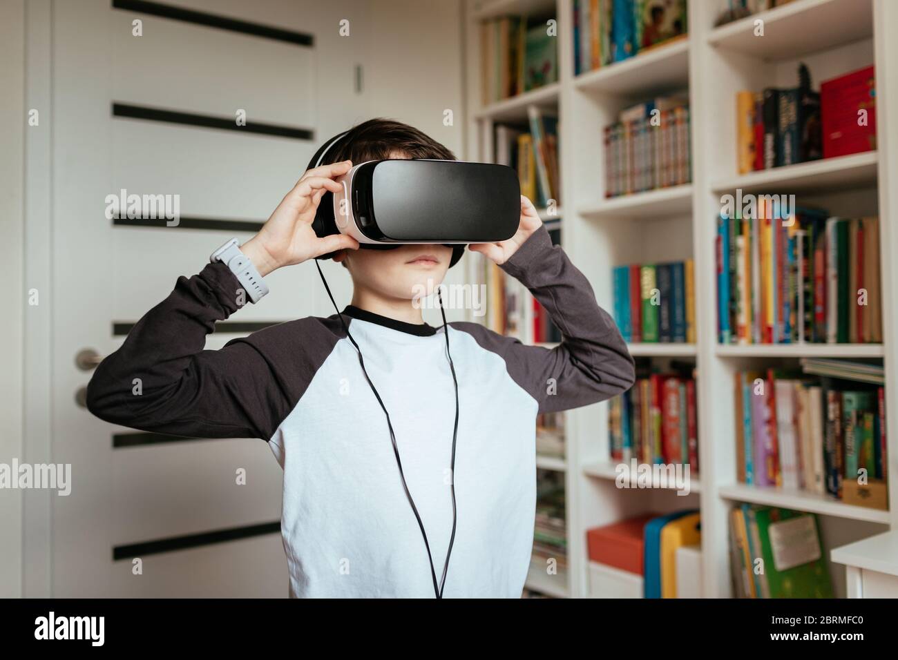 Junge, die VR-Brille mit Kopfhörern trägt. Mittlere Aufnahme eines Teenagers, der ein Virtual Reality-Headset trägt und berührt. Stockfoto