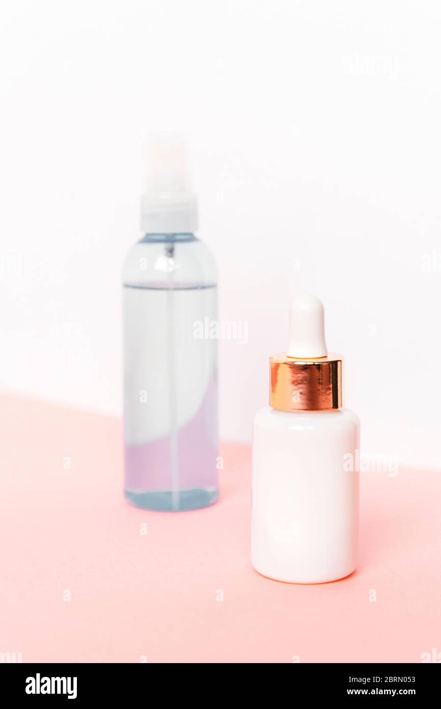 Zwei Flaschen mit Serum und Kosmetiklotion auf rosa Tisch gegen weiße Wand. Unbranded leere Pakete. Natürliche Hautpflegeprodukte Konzept. Stockfoto