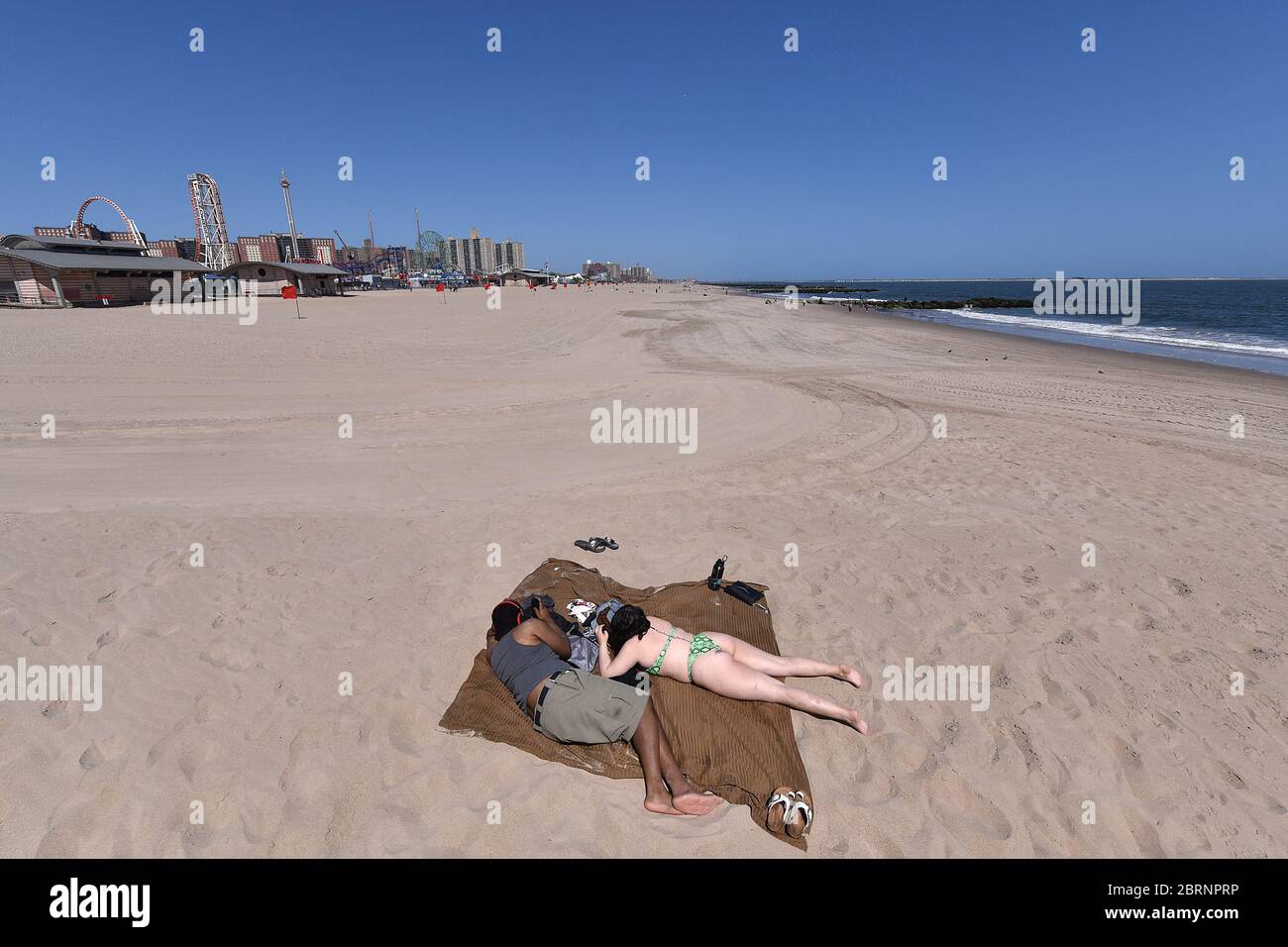 New York City, USA. Mai 2020. Ein Paar übt soziale Distanz, während sie an einem fast leeren Teil des Coney Island Strandes im Brooklyn-Bezirk von New York City, NY, am 21. Mai 2020 liegen. Die NYPD kündigte an, dass sie am Memorial Day Wochenende die Strände patrouillieren wird, um die soziale Distanz zu genießen und Masken auszuteilen, und sagte, Strandbesucher können nur knöcheltief ins Wasser gehen, kein Schwimmen ist erlaubt, aber Surfen wird erlaubt sein. (Anthony Behar/Sipa USA) Credit: SIPA USA/Alamy Live News Stockfoto