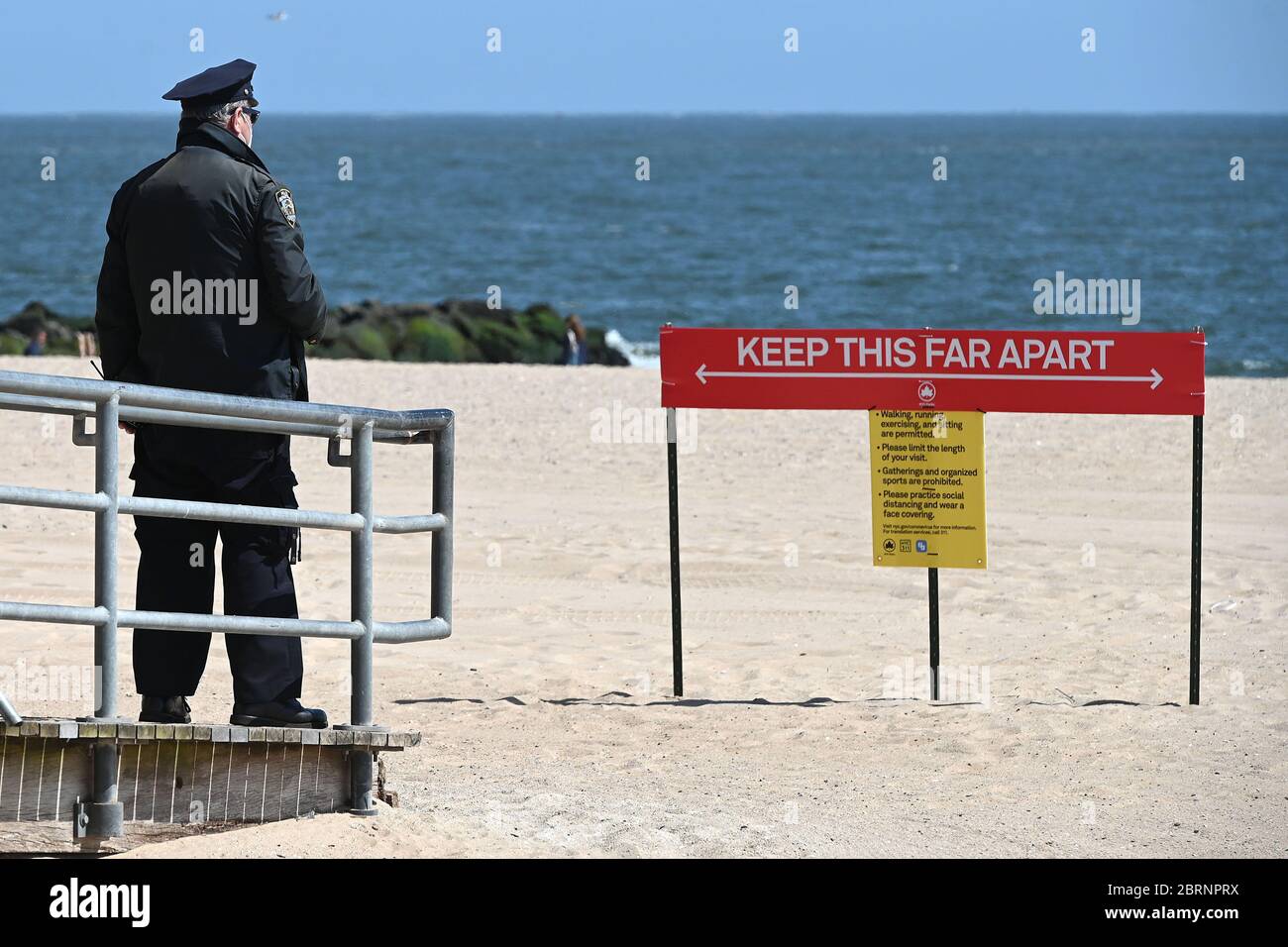 In der Zeit der COVID-19-Pandemie trägt ein NYPD-Offizier eine Gesichtsmaske und blickt auf den Strand vor der Strandpromenade von Coney Island, um die sozialen Abwehrregeln zu wahren und schützende Gesichtsmasken auszuhändigen.im Brooklyn-Bezirk New York City, NY, 21. Mai 2020. Die NYPD kündigte an, dass sie am Memorial Day Wochenende die Strände patrouillieren wird, um die soziale Distanz zu genießen und Masken auszuteilen, und sagte, Strandbesucher können nur knöcheltief ins Wasser gehen, kein Schwimmen ist erlaubt, aber Surfen wird erlaubt sein. (Anthony Behar/Sipa USA) Stockfoto