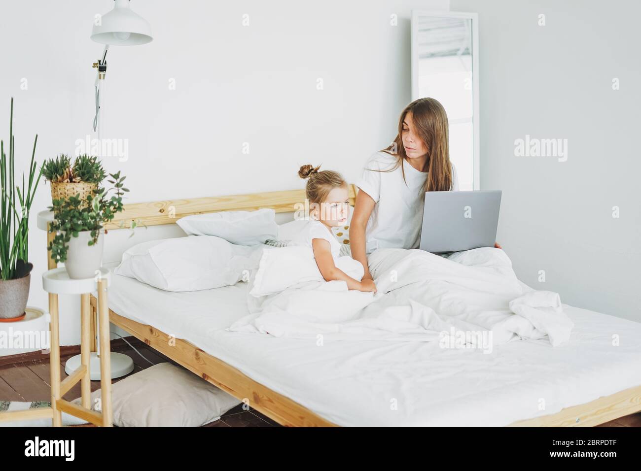 Strenge Mutter Freelancer mit kleinen Tochter wollen auf Laptop im Bett in hellen Innenraum zu Hause arbeiten Stockfoto